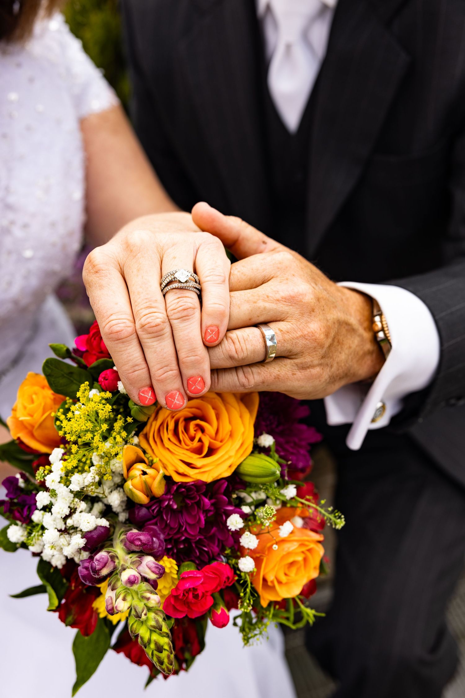 Close-up of couple's hands showing wedding rings, wedding commitment of rings and lifetimes with beautiful flowers from California wedding.