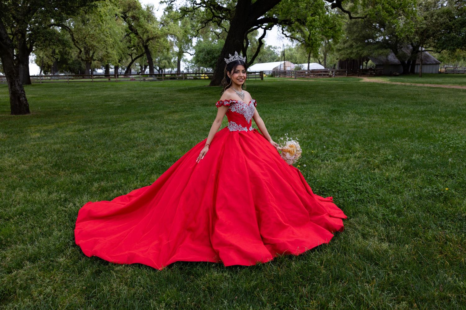 A person in a flowing red dress twirls gracefully on a lush green lawn surrounded by trees.