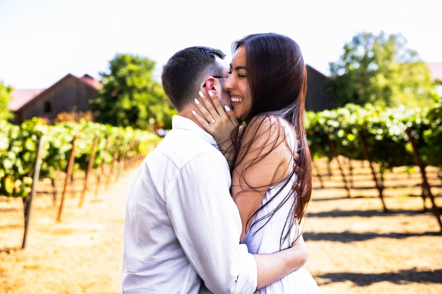 Two people share a romantic moment in a sun-drenched vineyard with rows of grapevines in the background.