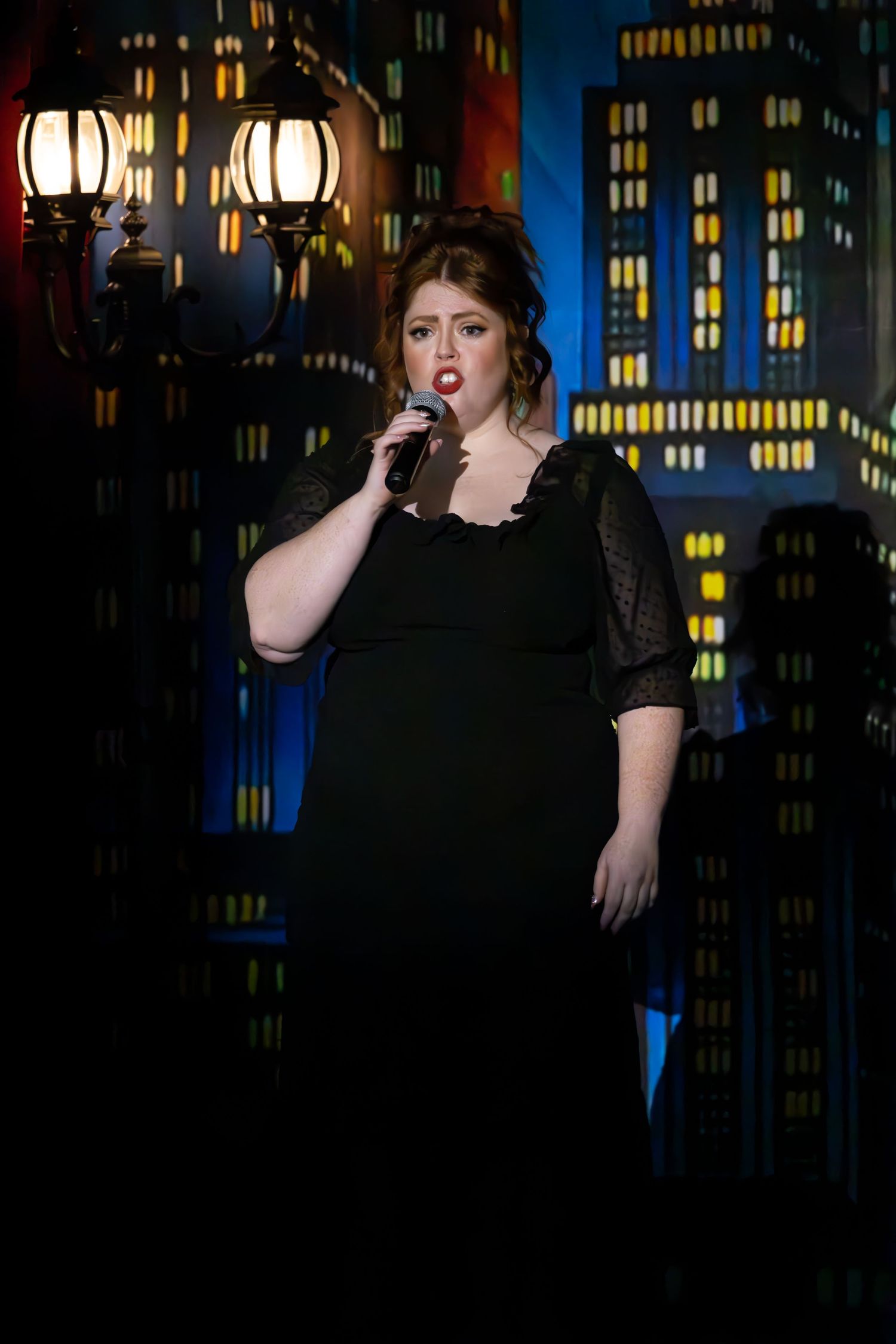 Performance on stage against a cityscape backdrop with glowing windows and street lamps creating an urban nighttime atmosphere.
