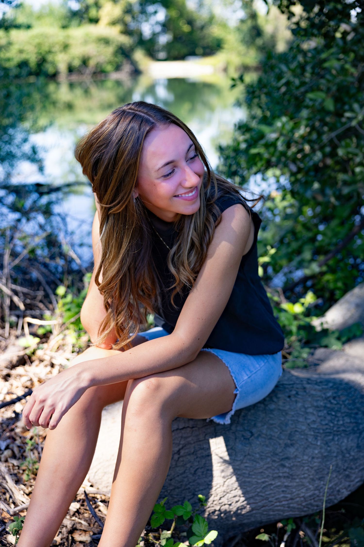 Smiling senior girl sitting on a log by the water at Lodi Lake — casual, natural light, and relaxed spring senior portrait vibes.