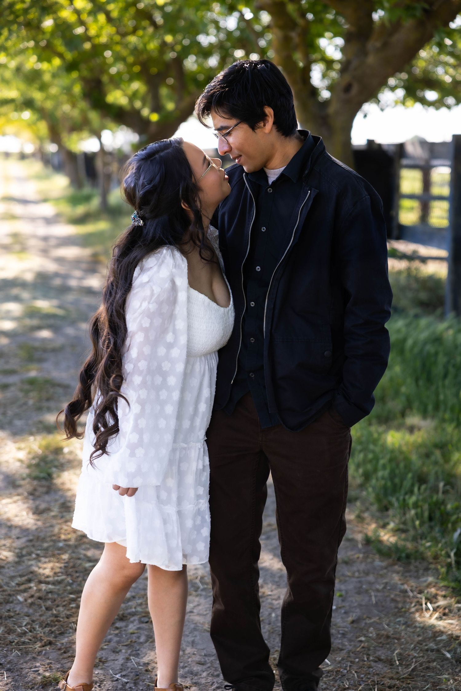 A romantic couple shares tender moments in a sunlit outdoor setting with trees and grass in the background.