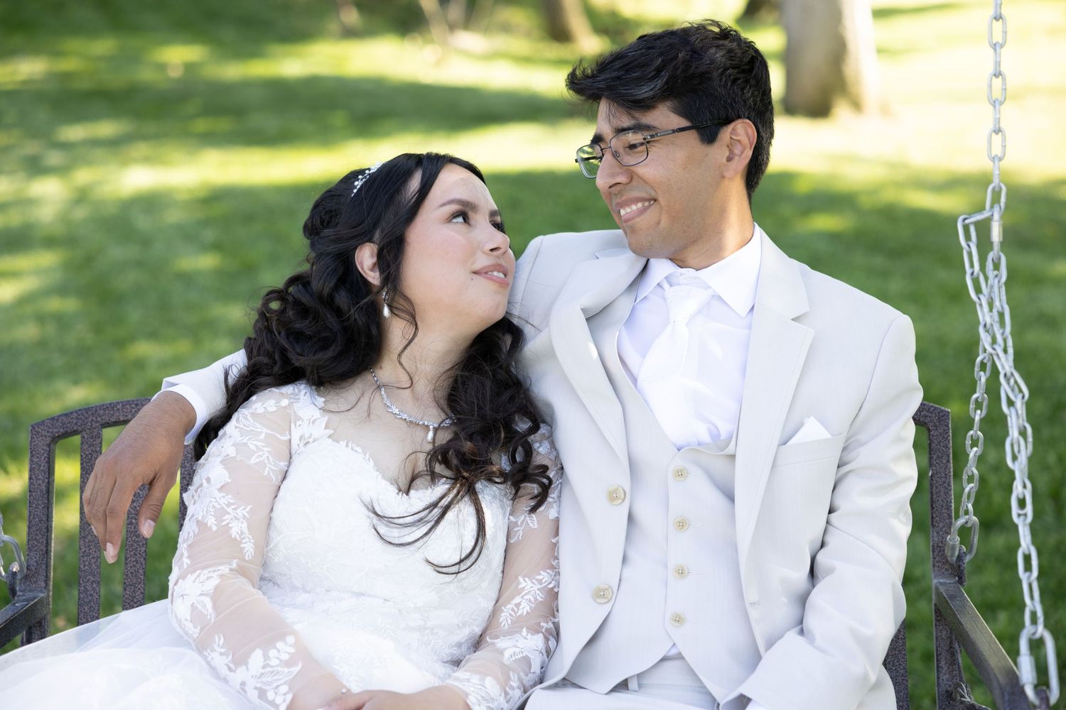 Newlyweds share a tender moment while sitting on a swing in a sunny garden setting.
