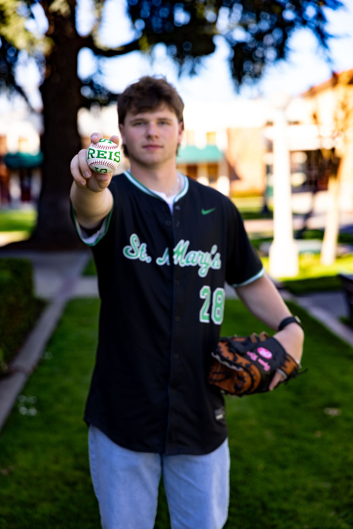 A Saint Mary's baseball player in a dark jersey shows off a signed baseball in an outdoor setting in Downtown Lodi.  Stockton