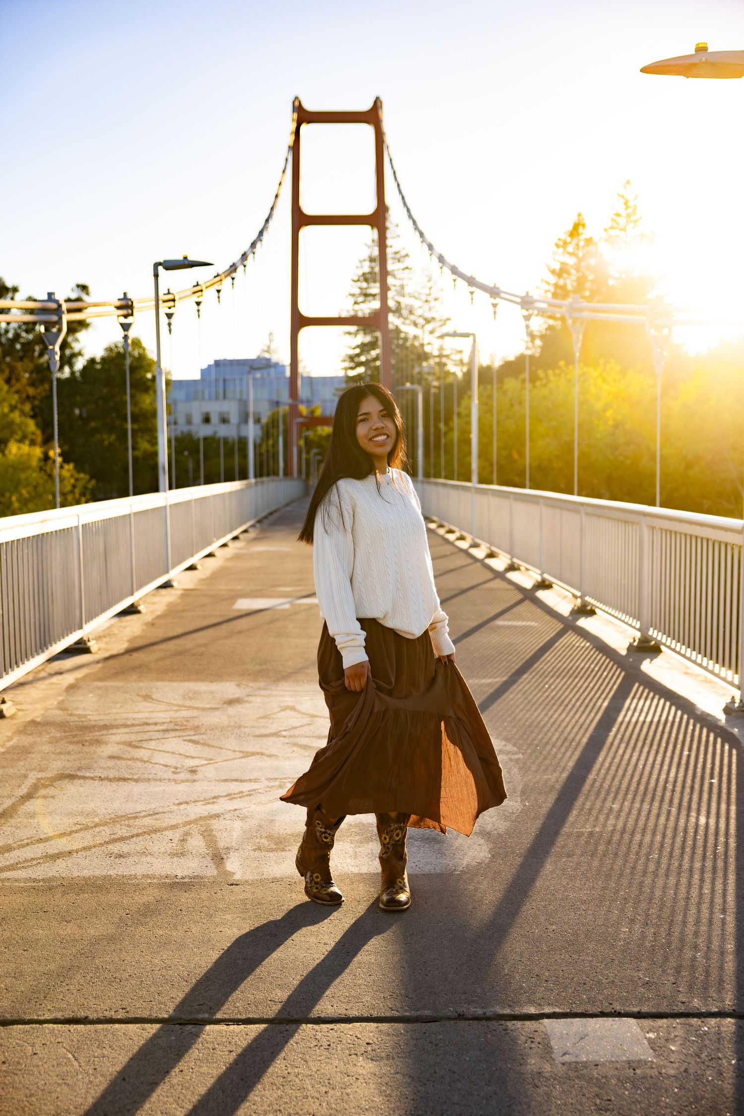 Senior in white sweater on suspension bridge at golden hour, guy west bridge in Sacramento, California