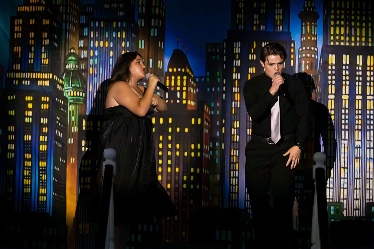 Stage backdrop depicting illuminated night city skyline with glowing windows and skyscrapers in blue tones.