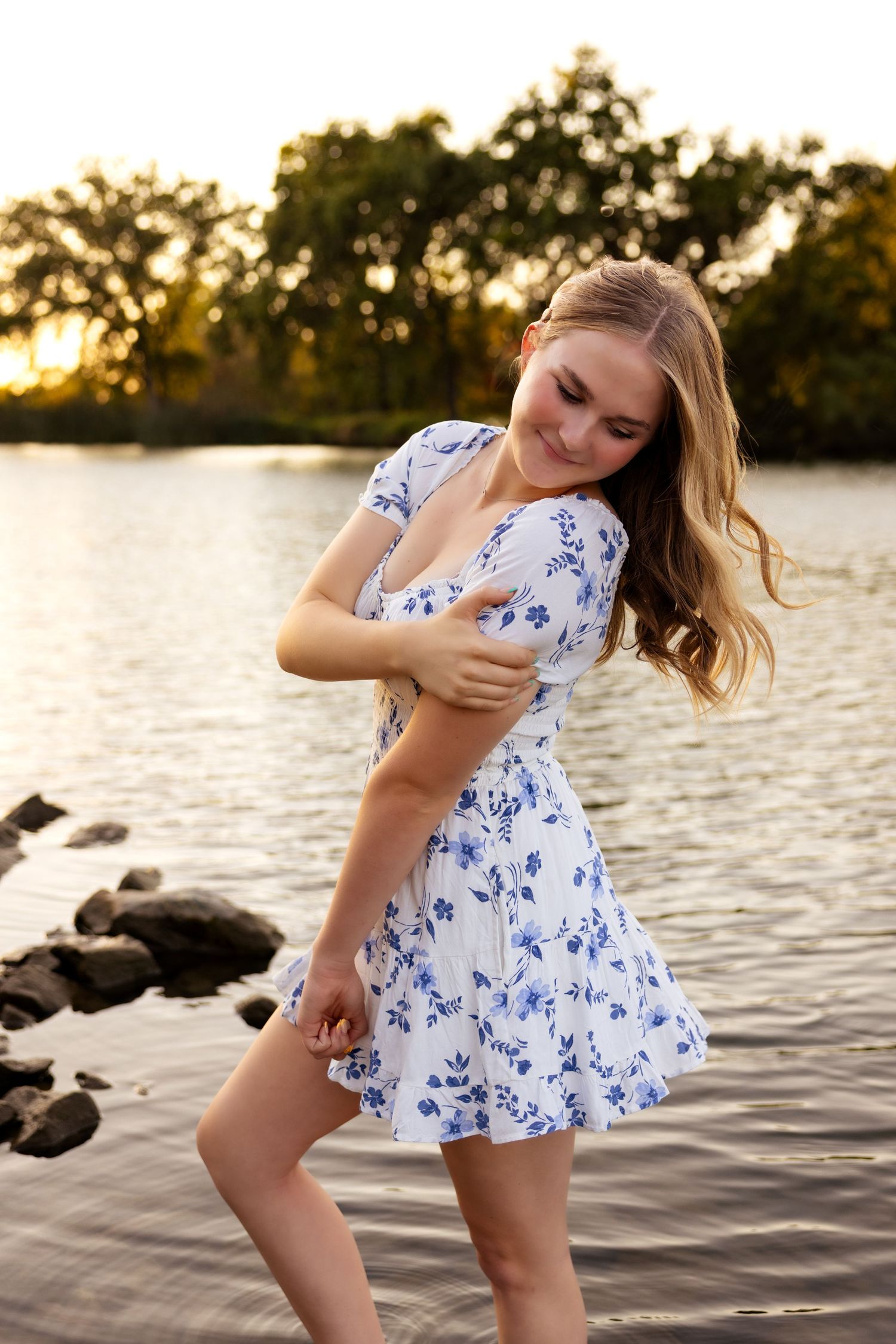Senior girl in a white and blue floral dress by the water at sunset — soft light, spring vibes, and perfect Lodi Lake senior portrait settin
