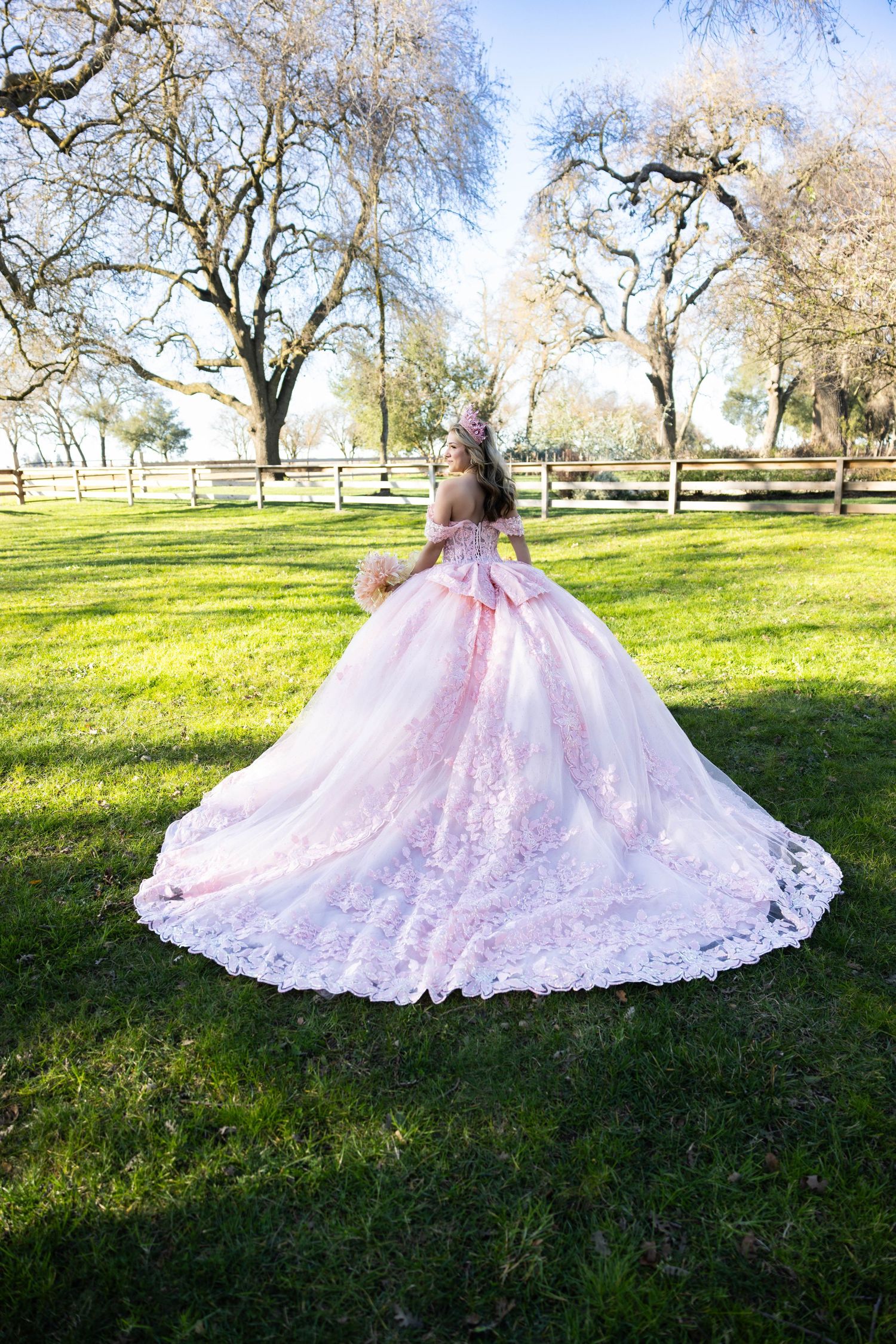 A pink quinceañera gown with lace details captured spinning in a sunlit garden with bare trees with beautiful surroundings at Jesses Grove W