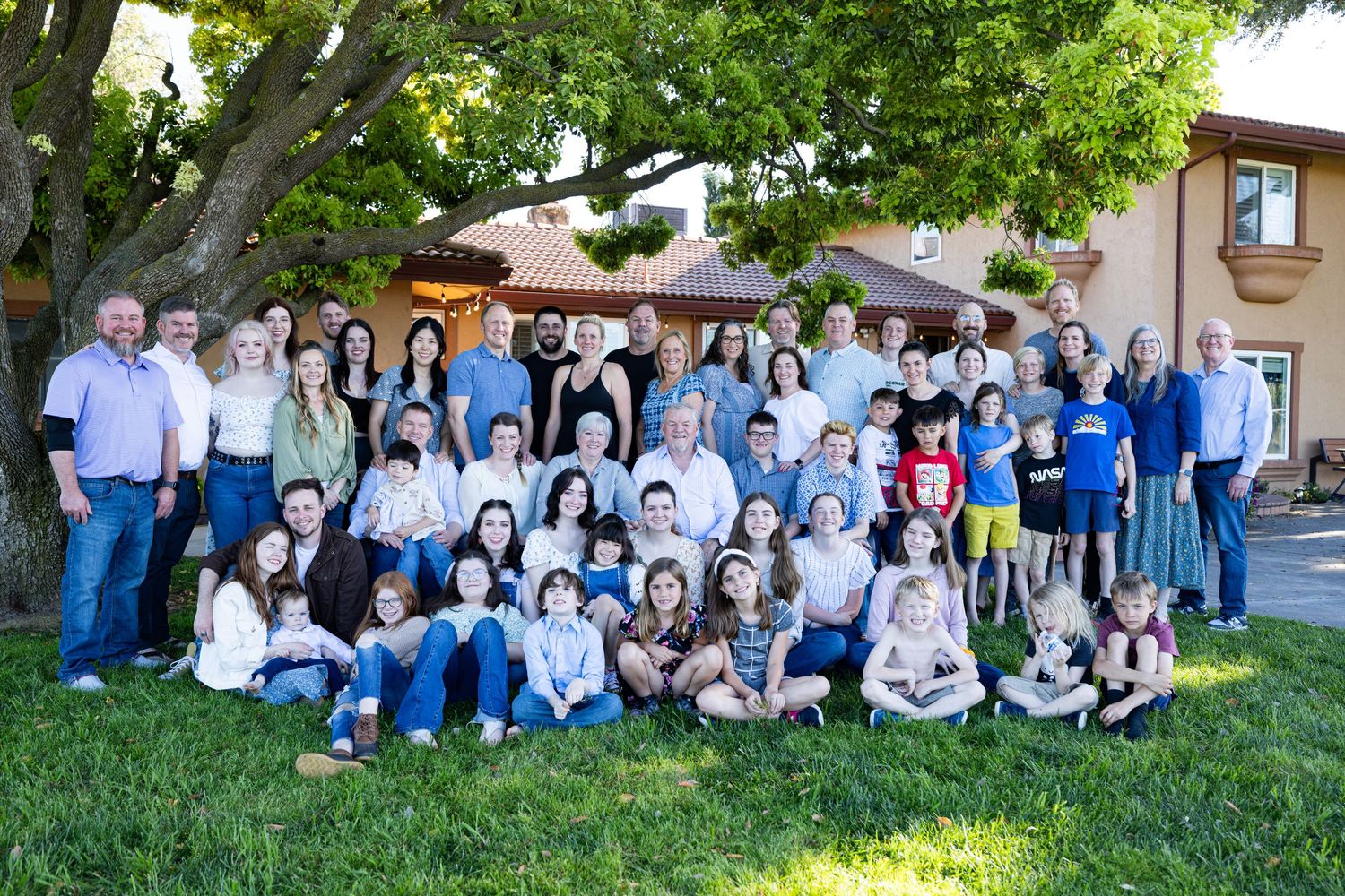 Large group photo of people gathered outdoors under a tree on a sunny day in Acampo.
