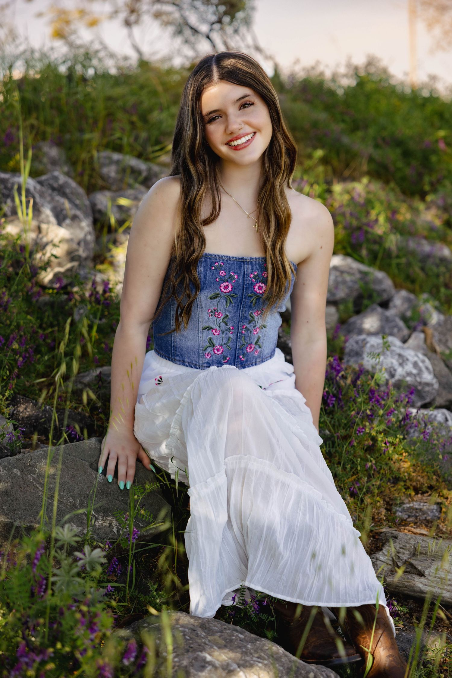 A denim corset top with floral embroidery paired with a flowing white skirt in a wildflower meadow at sunset.