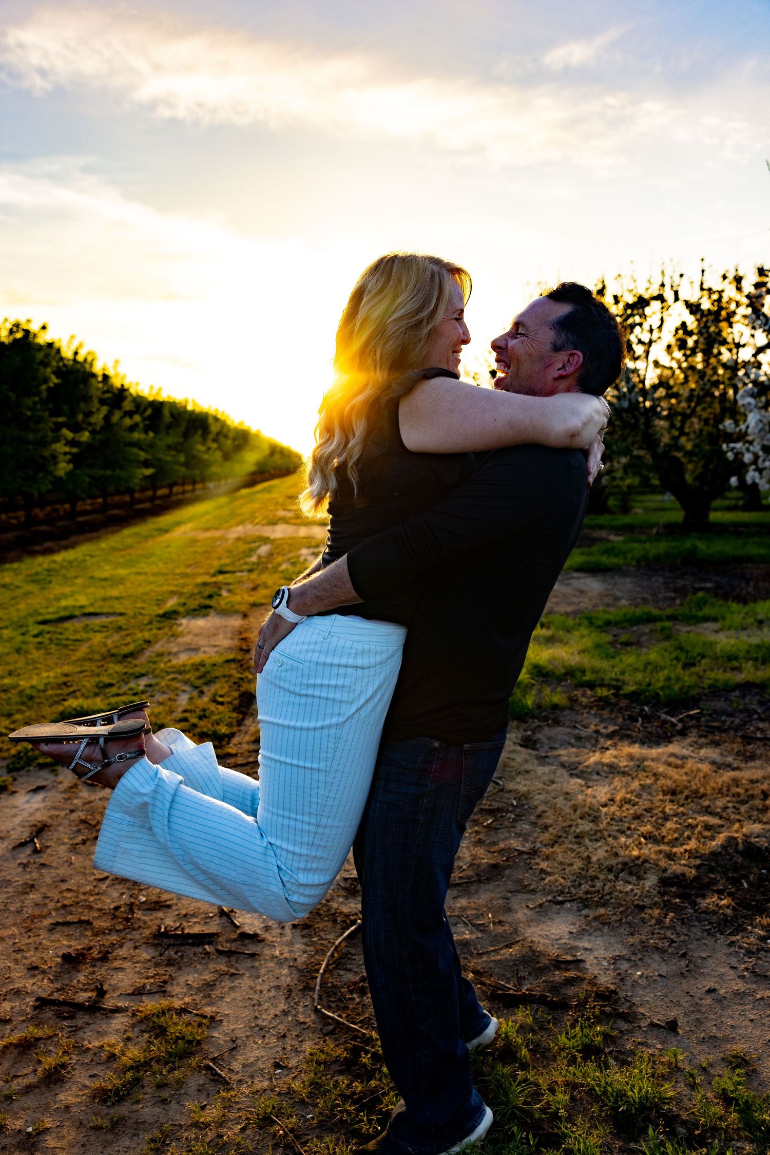 A couple embraces in a romantic spin against a golden sunset in an orchard setting.