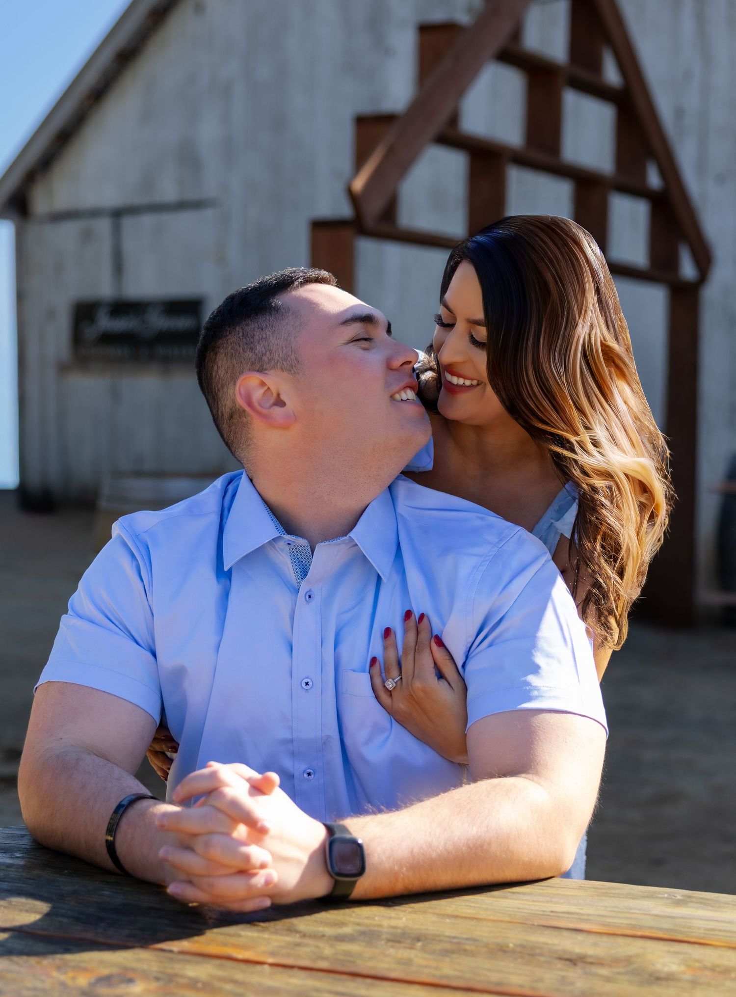 Couple sharing romantic moments at a rustic wooden table in matching light blue shirts.