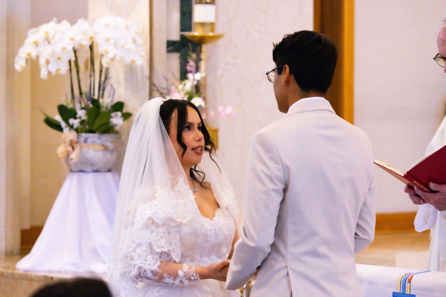 A couple stands together at their wedding ceremony with white orchid decor in the background.