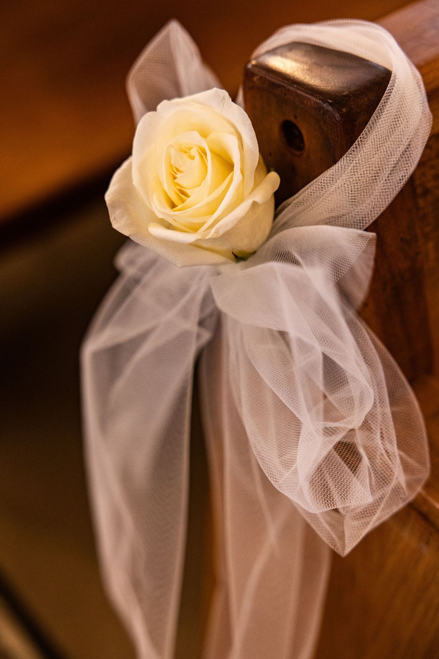 A cream colored rose adorns a white tulle veil draped elegantly over a wooden chair back.