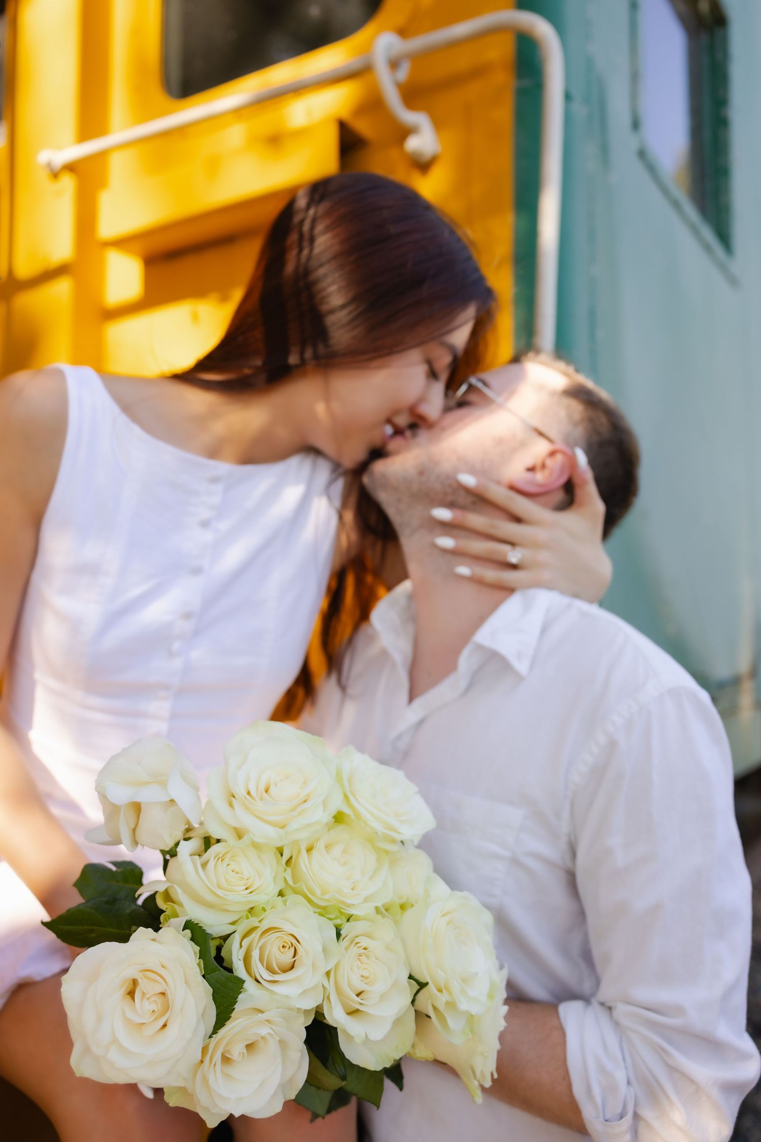 A romantic wedding couple embracing while holding a bouquet of white roses against a bright yellow background.