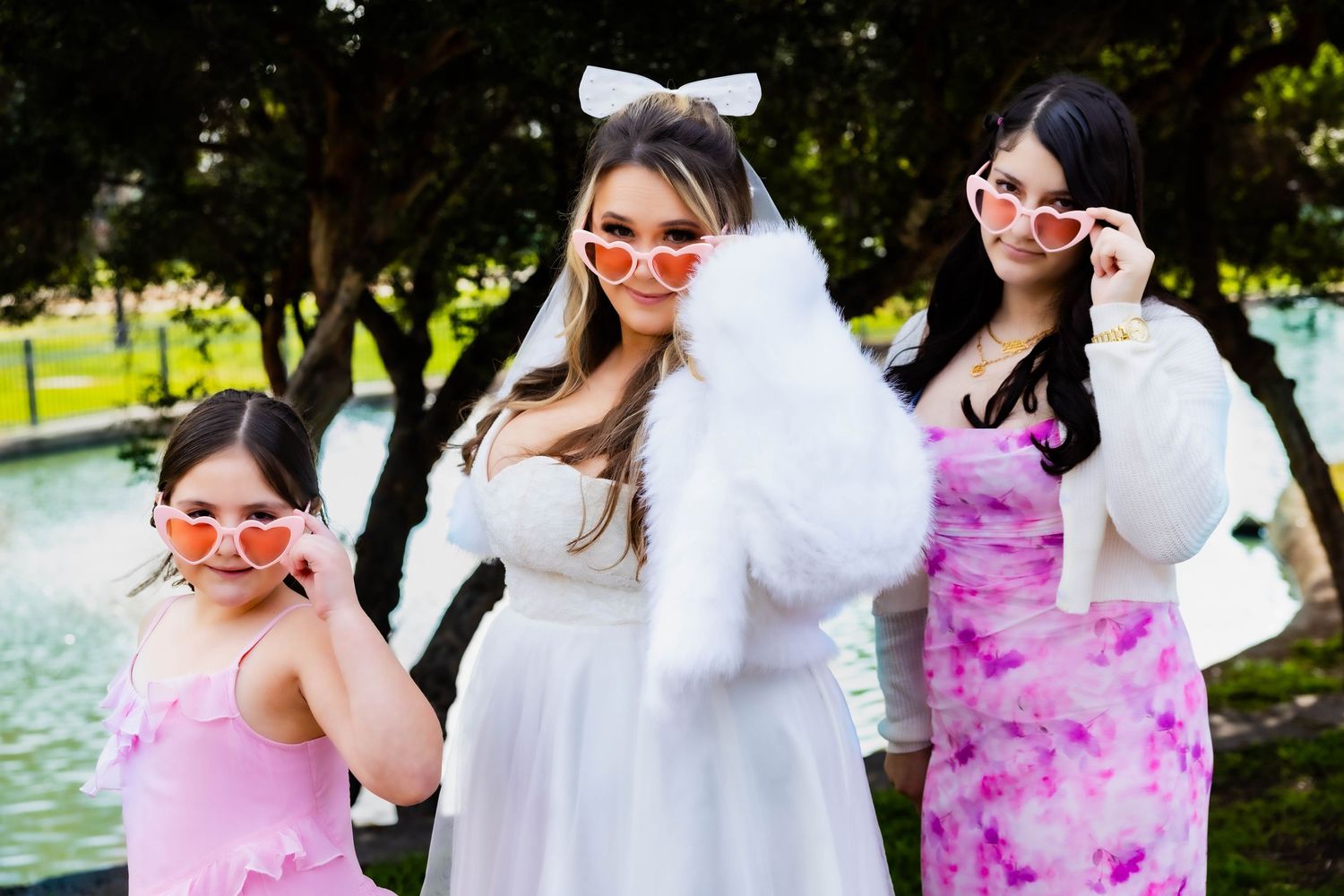 Three friends in colorful dresses and sunglasses pose playfully by a pond.