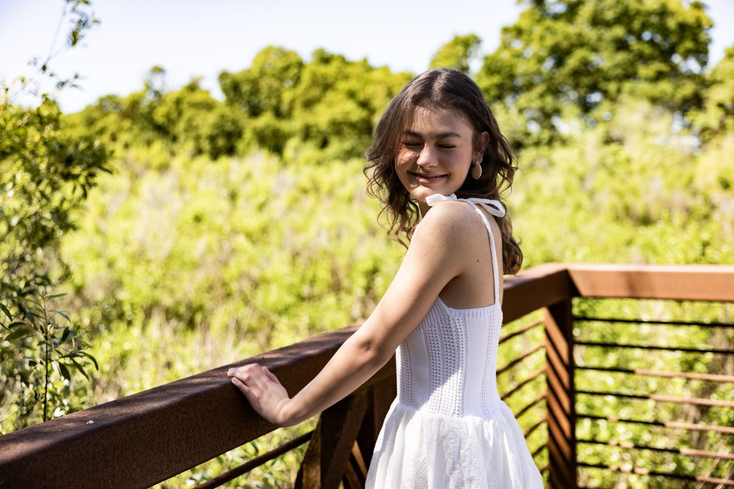 Senior girl in a white dress on a bridge at Lodi Lake — sunlit spring day, natural greenery, and classic senior portrait charm. Katie Malind