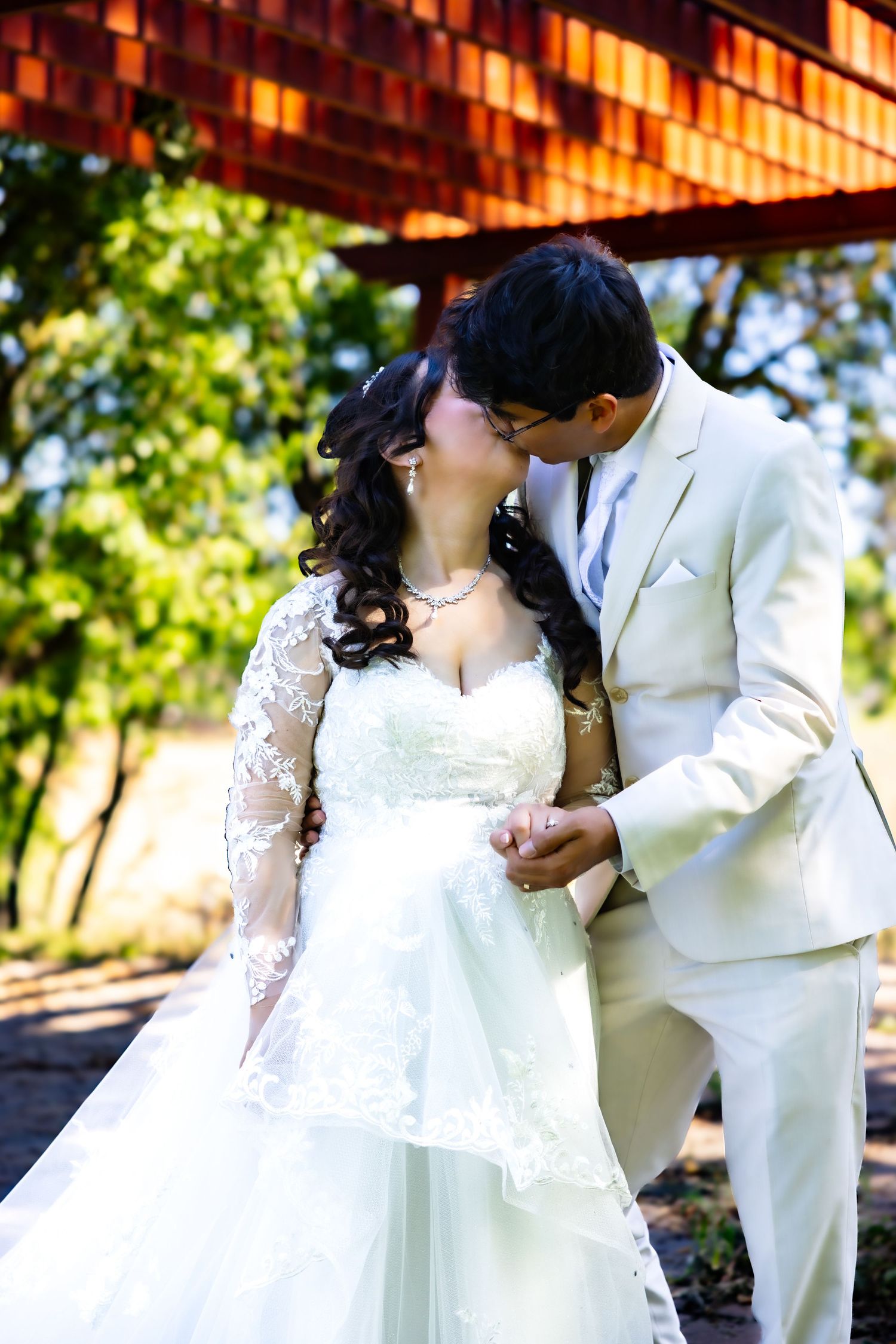 A romantic wedding couple in white attire share intimate moments in a sunlit outdoor setting.
