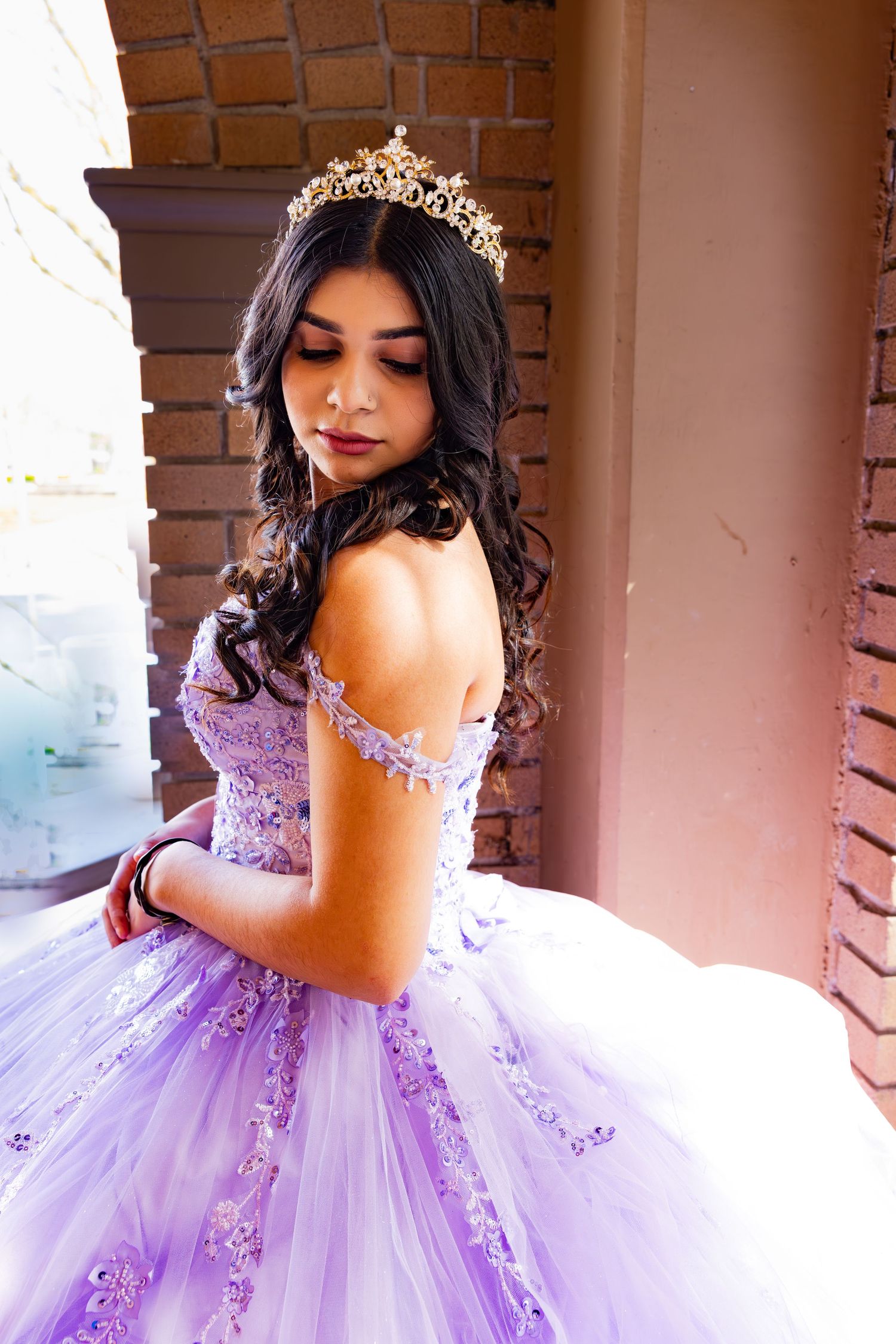 A lavender quinceanera dress with delicate lace details and a voluminous tulle skirt is showcased in an outdoor setting.