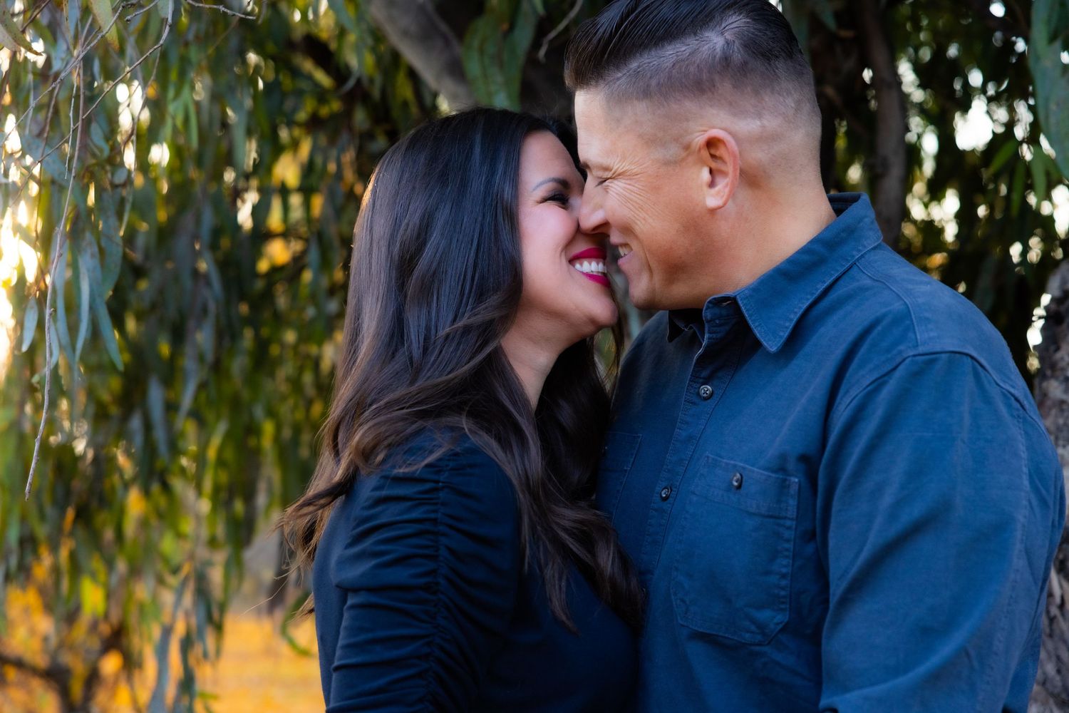 Romantic couple sharing intimate moment under willow tree at sunset, kissing and eloping.
