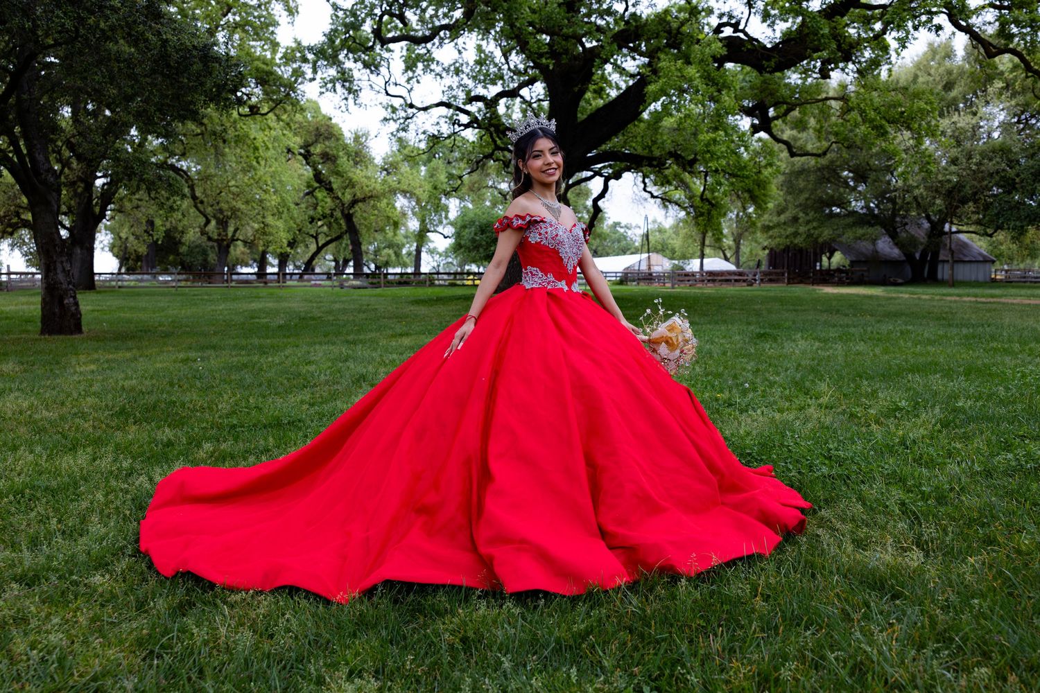 A flowing red dress creates a dramatic trail across a grassy hillside in a park setting.