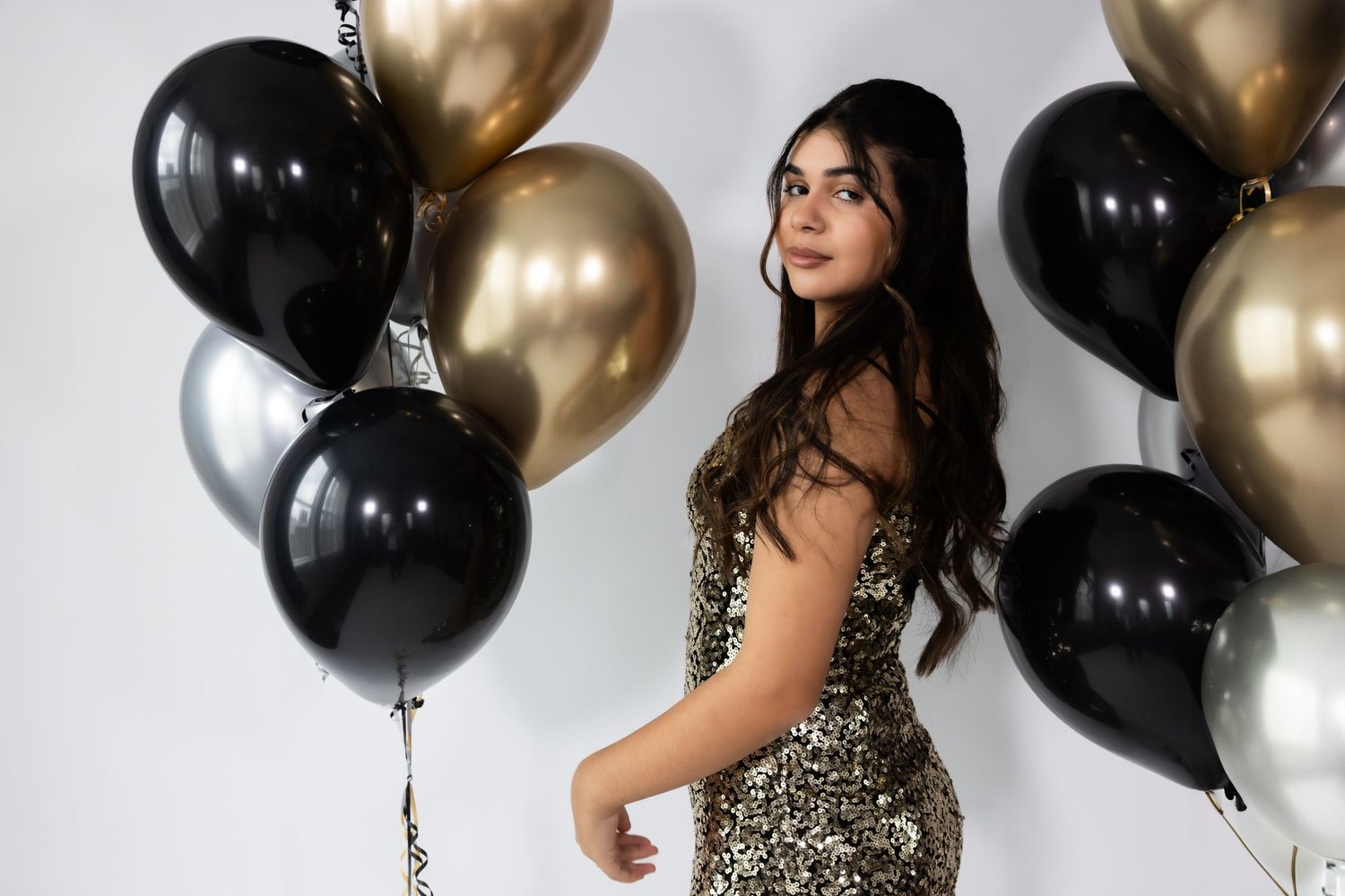 Glamorous party scene with black and gold balloons against white backdrop.