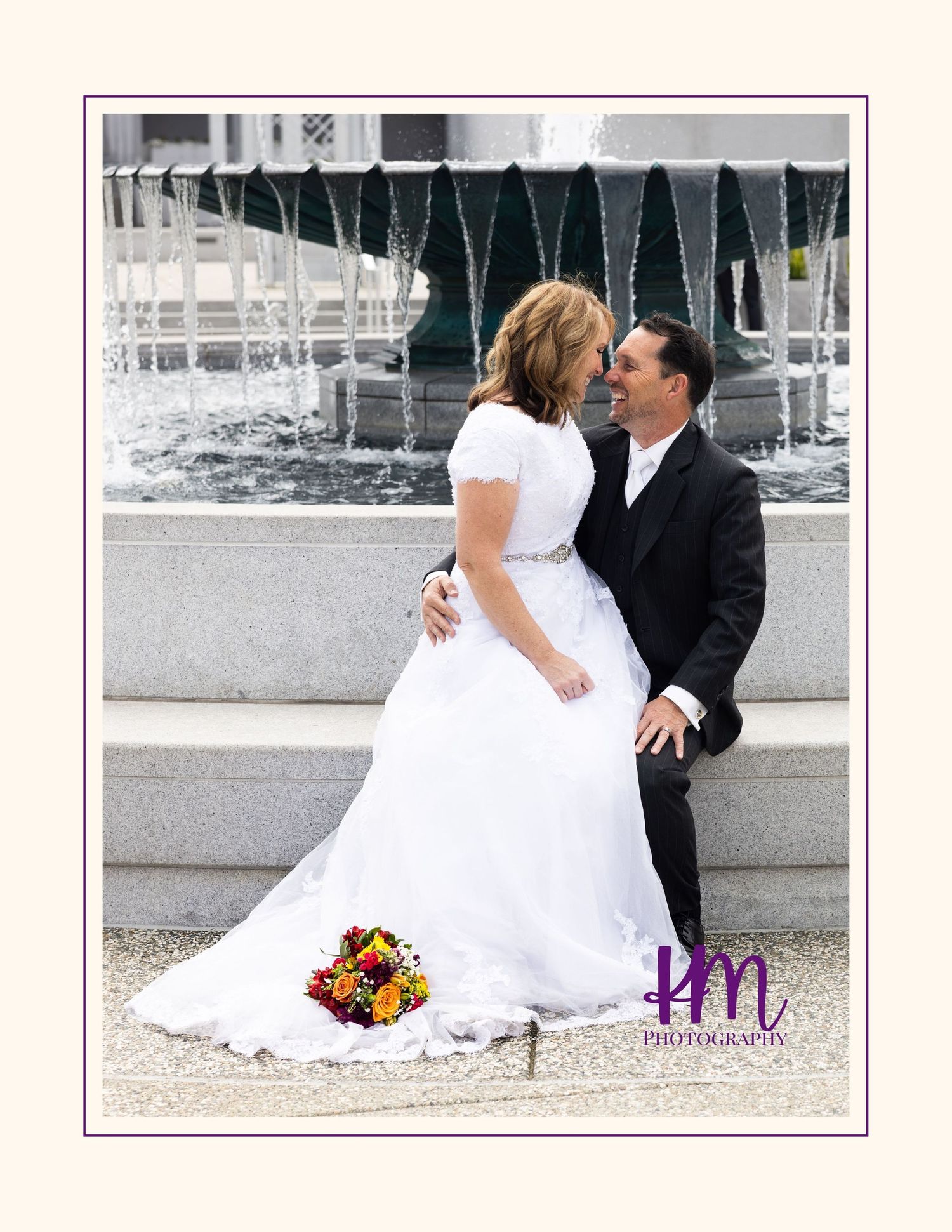 A bride and groom share a romantic moment while sitting by a fountain, with a colorful autumn bouquet beside them.