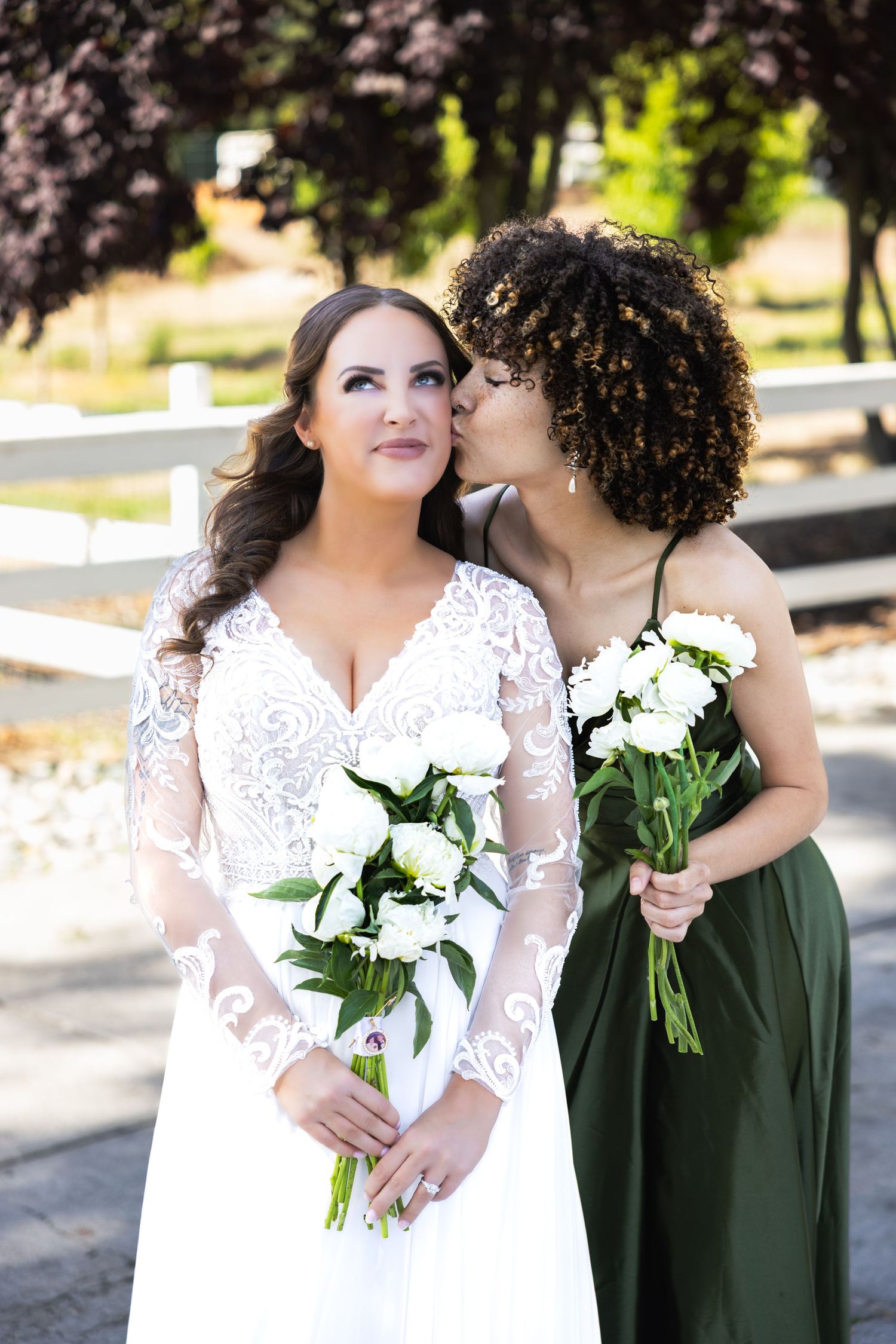Two people in wedding attire share an intimate moment while holding white floral bouquets outdoors.