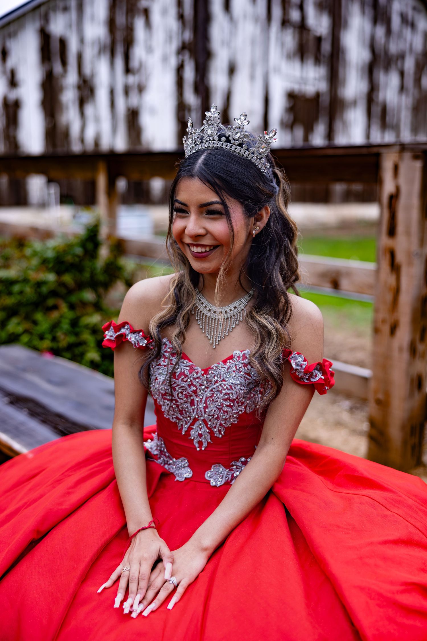 An ornate red quinceañera gown with crystal details and tiara photographed against weathered wood barn in Sacramento Valley by Katie Malinda