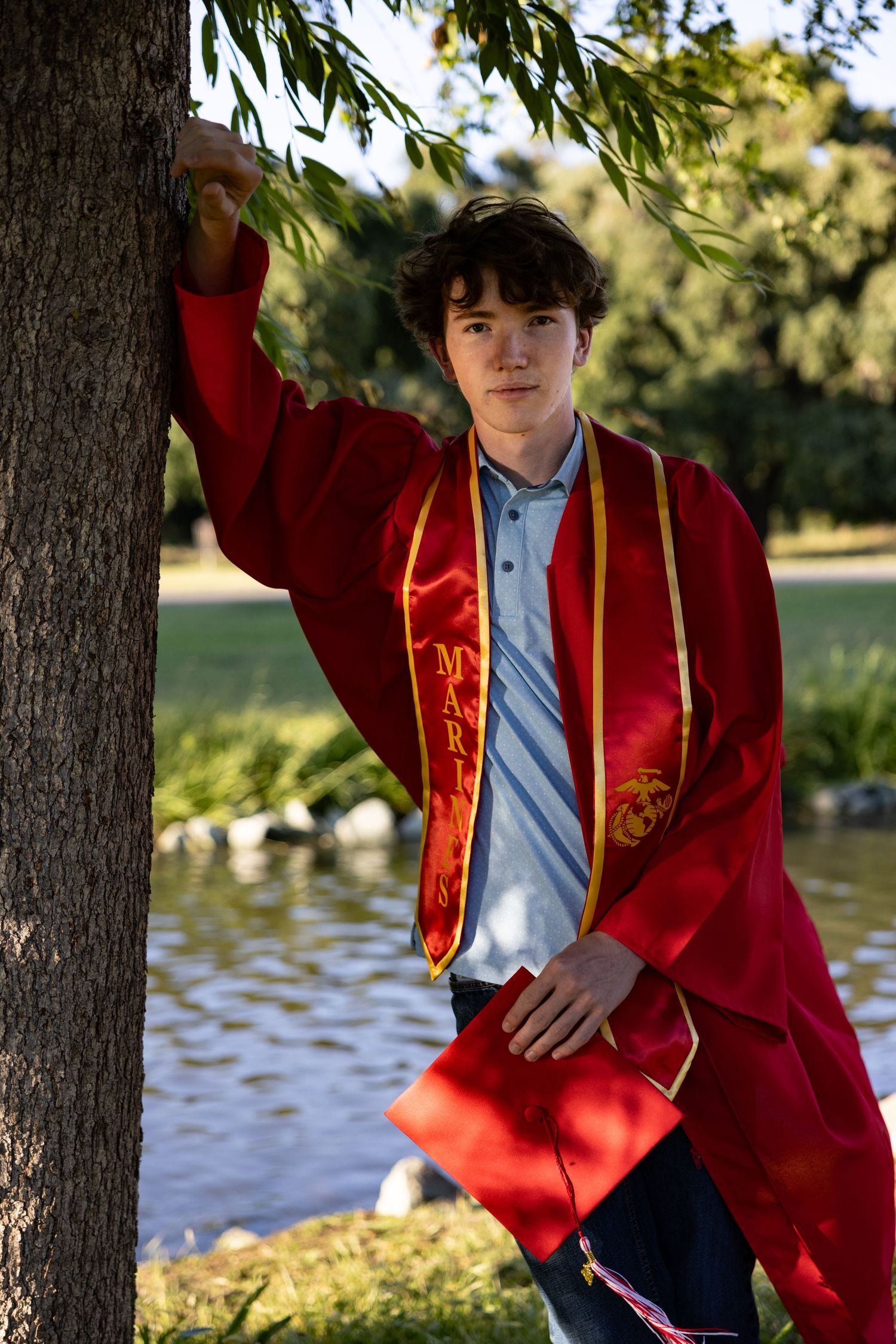 A red graduation gown worn casually while leaning against a tree near a Lake in Stockton.
