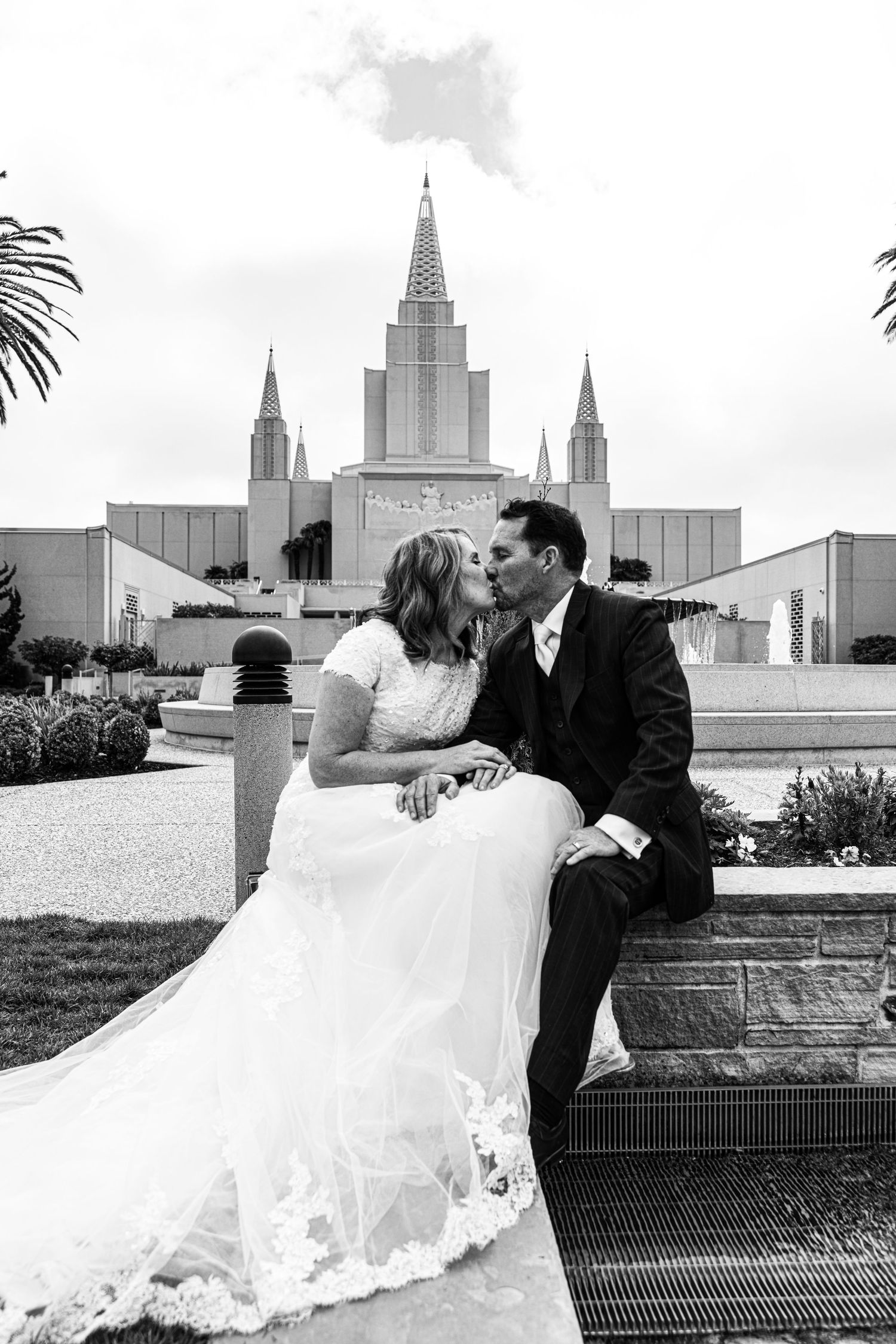 A black and white wedding photo of a couple sitting on stone steps in front of the Oakland California LDS Temple.