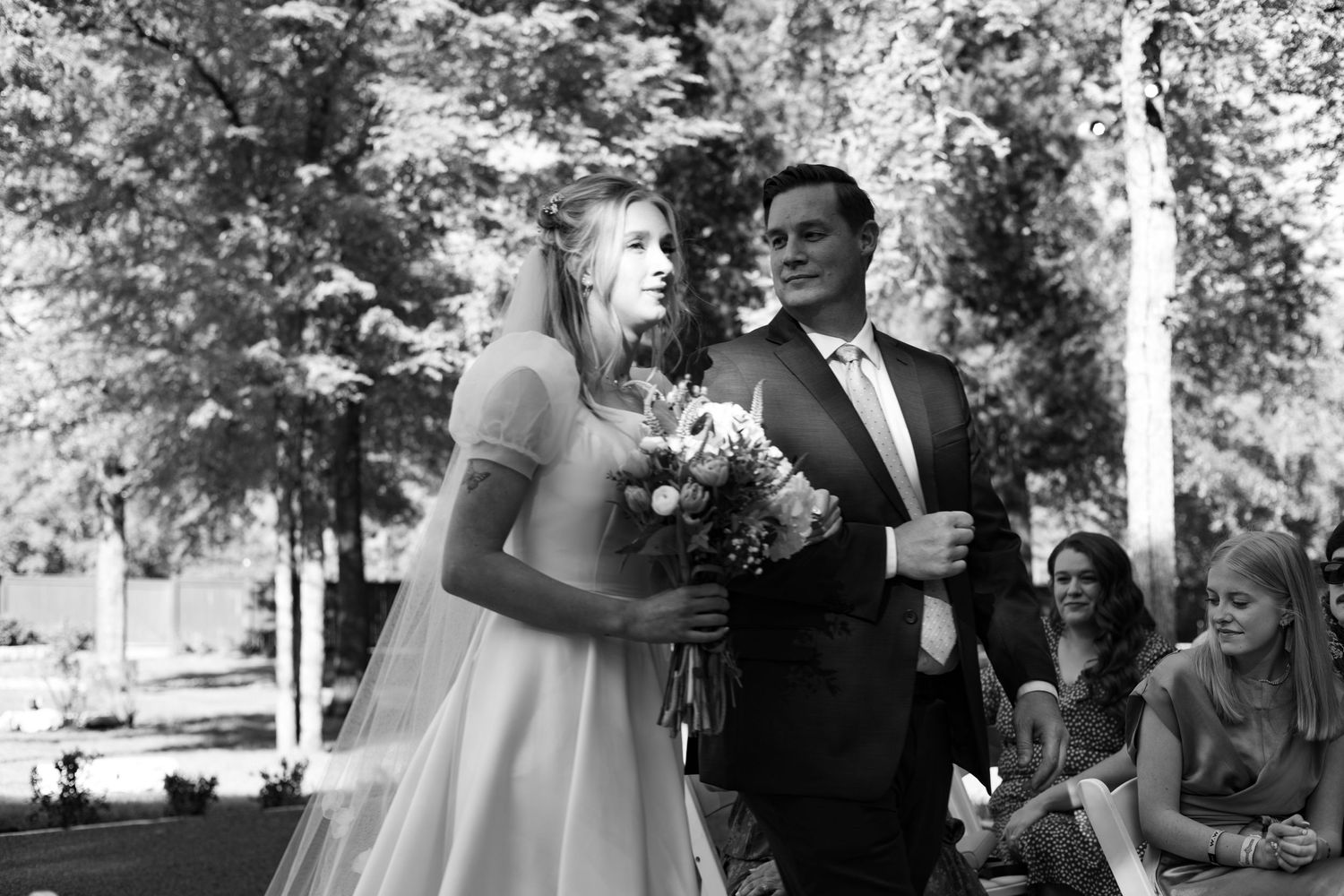Black and white wedding ceremony photo with floral bouquet as father walks bride down isle in Sacramento wedding.