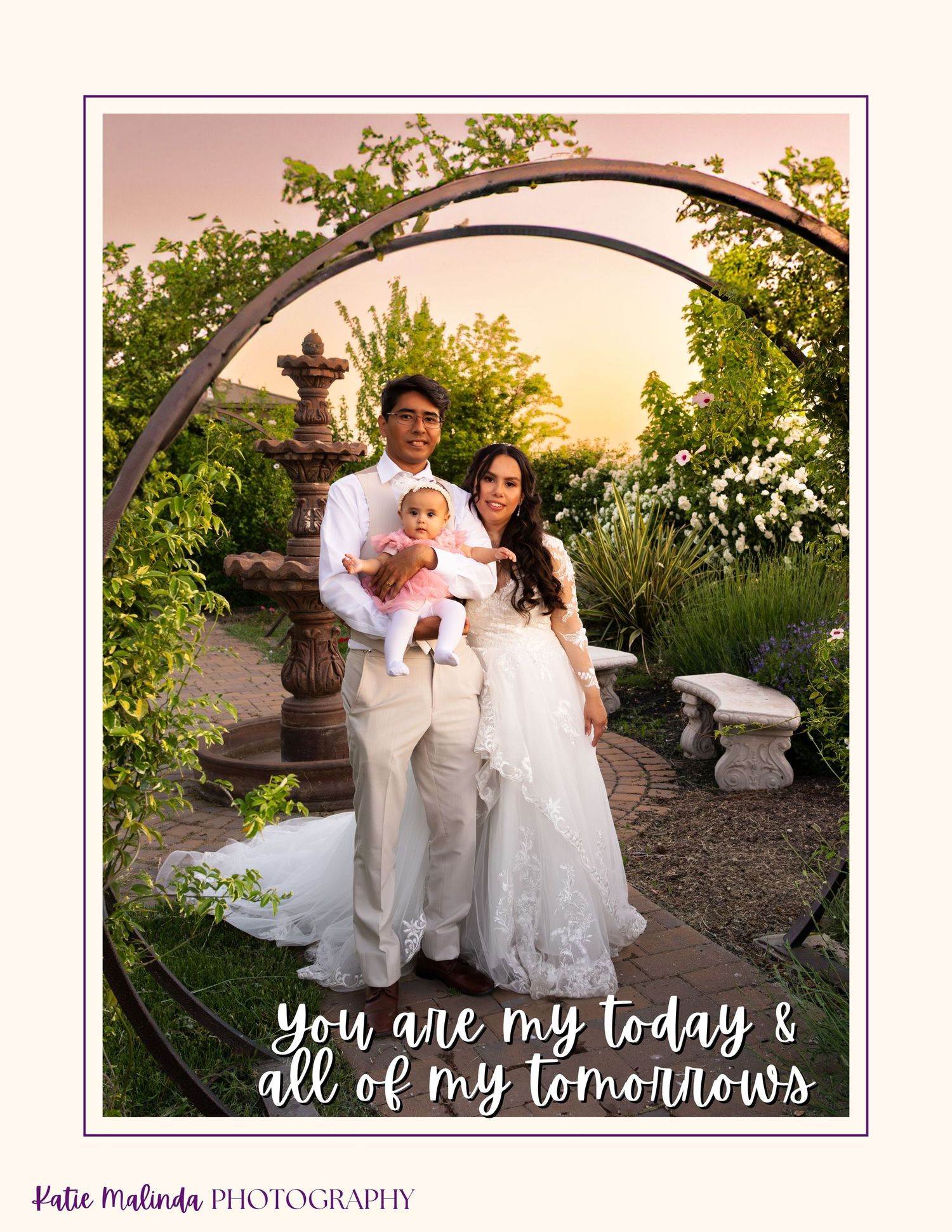 A romantic garden scene with a couple standing under a circular arch at sunset with white blooms and greenery.