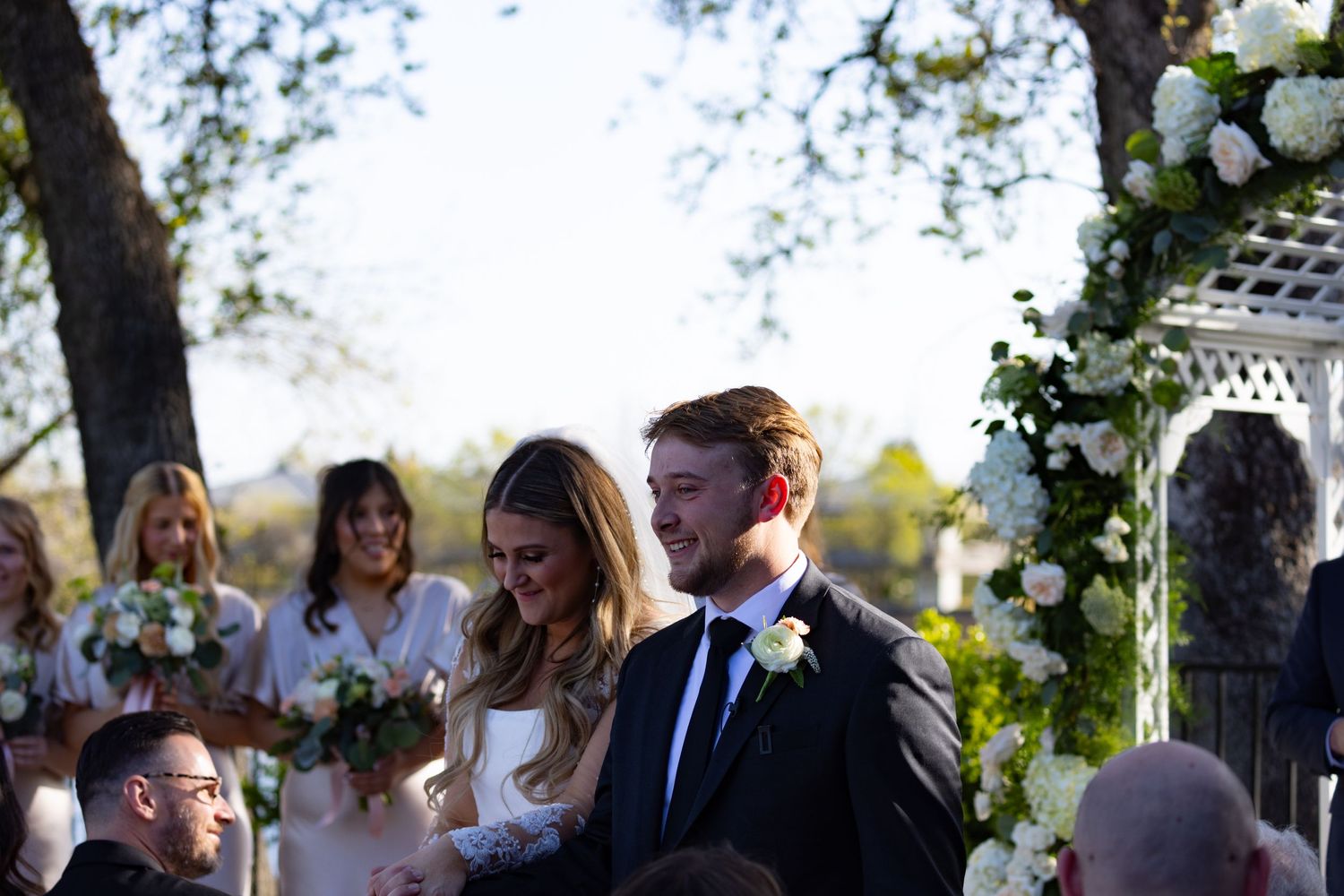 Romantic outdoor wedding in Chico, CA captured by Katie Malinda. First kiss under a floral arch—timeless, elegant, unforgettable moment.