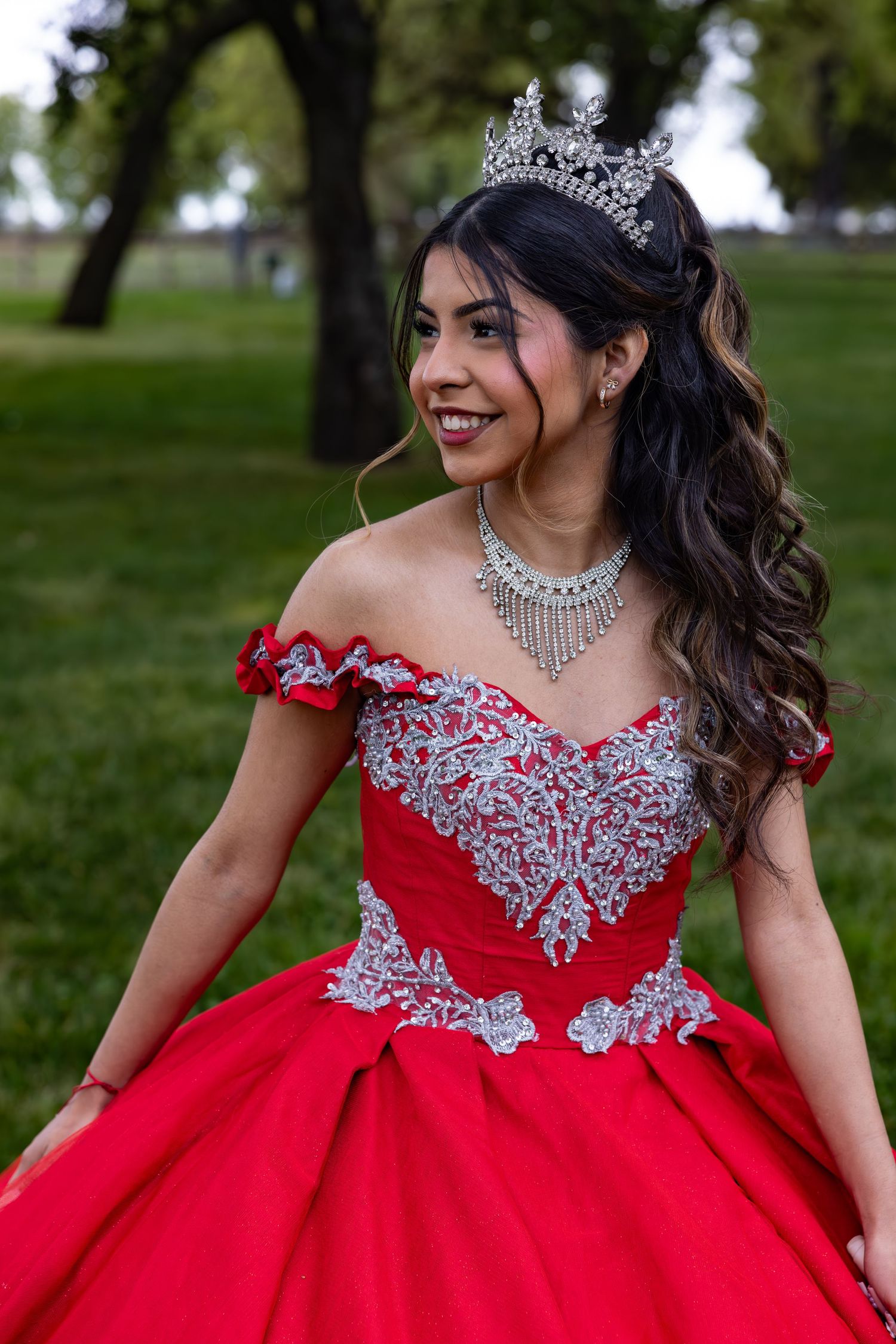A stunning red ball gown with silver beaded embellishments and off-shoulder design photographed in an outdoor setting.