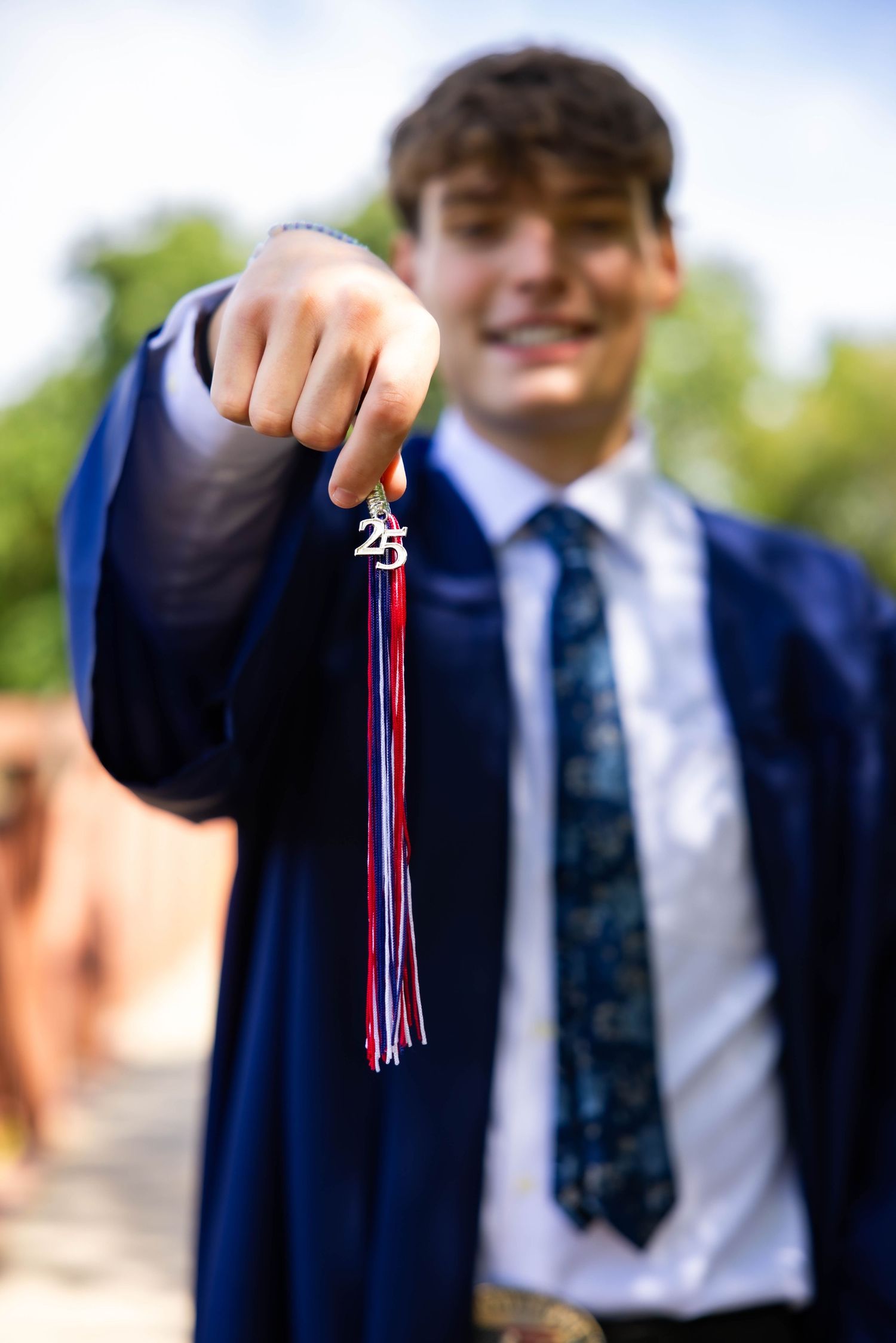 Senior boy holding Class of 2025 memorabilia in a navy blue graduation gown holding a graduation cap and tassel.