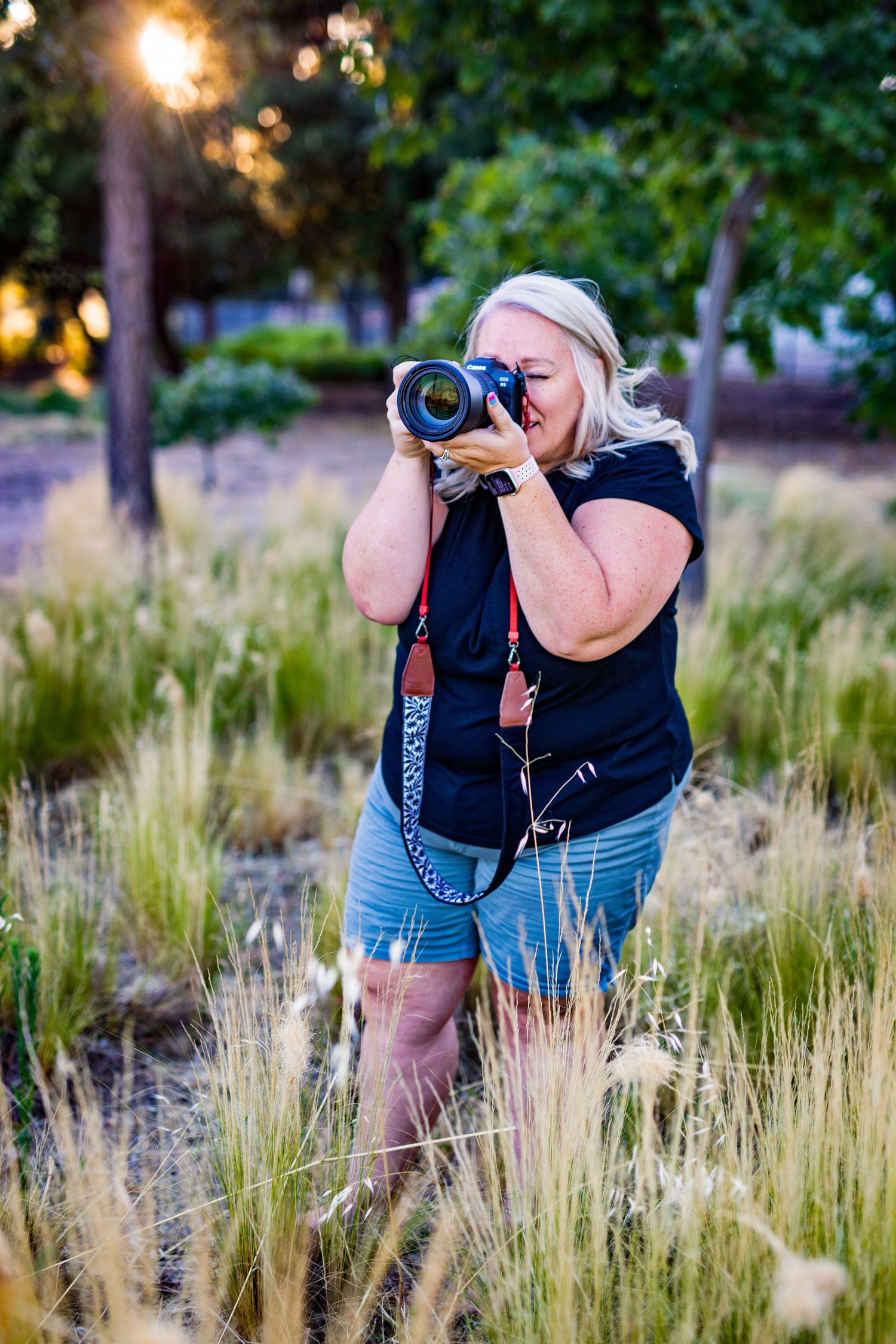 Photographer in blue shorts captures nature photos in tall grass field at golden hour.