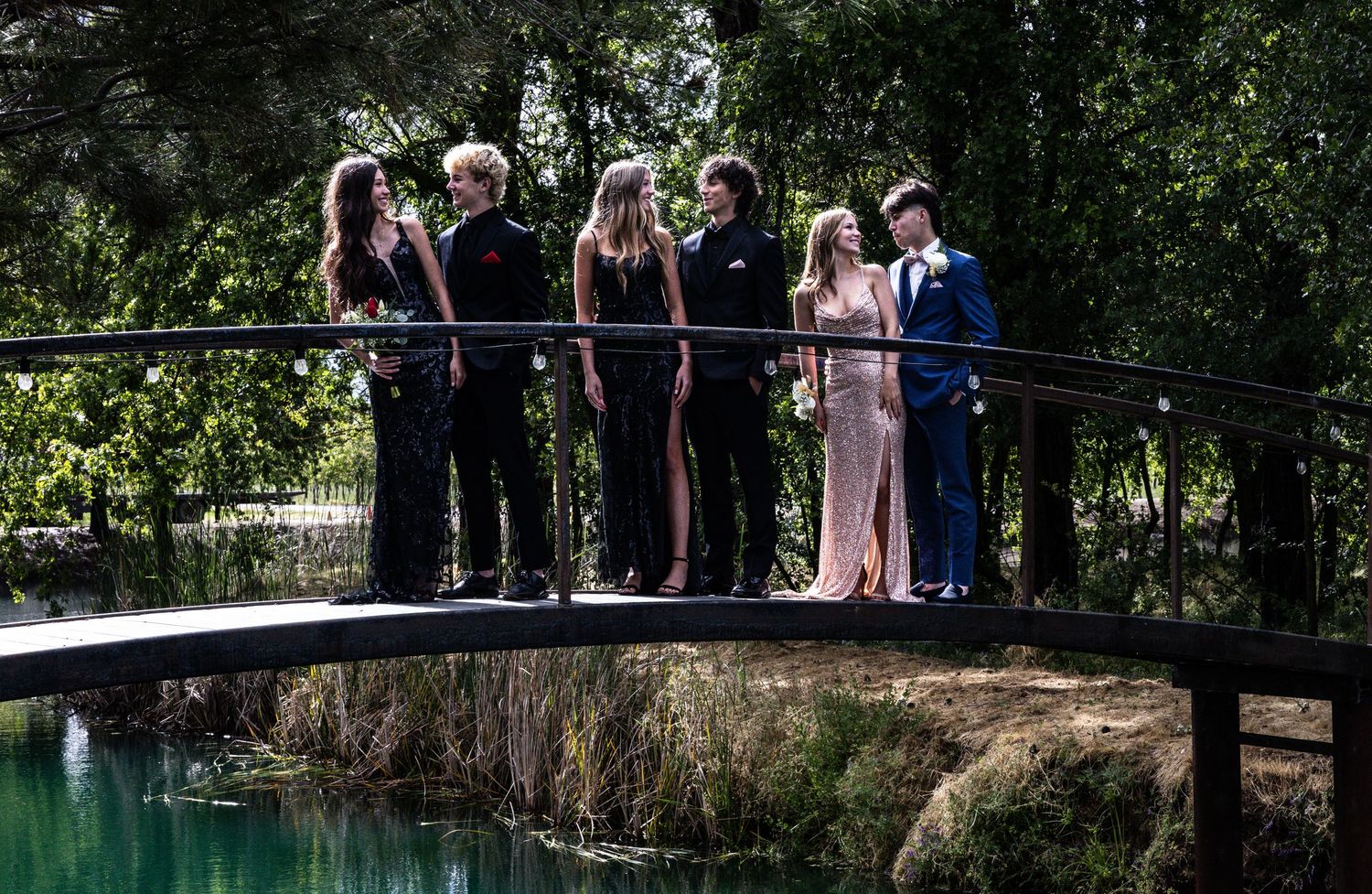 A group poses together on a wooden bridge over water during a formal event.