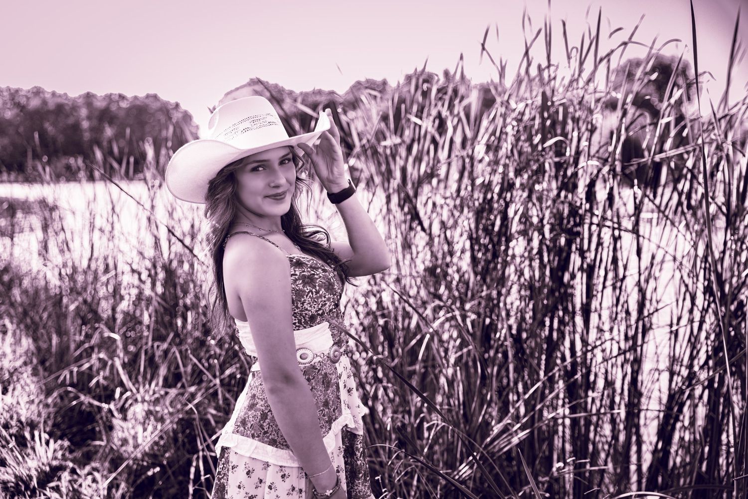 A person in a white hat walks through tall grass and wildflowers in a dreamy black and white photograph.