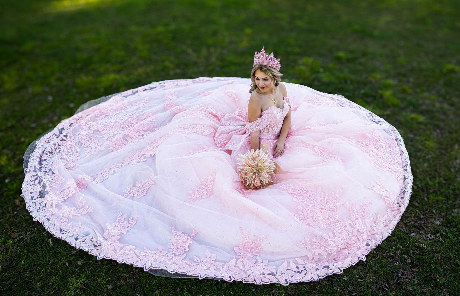 A pink quinceañera gown creates a perfect circle spread out on grass with delicate lace details for a photographer like Katie Malinda Photog