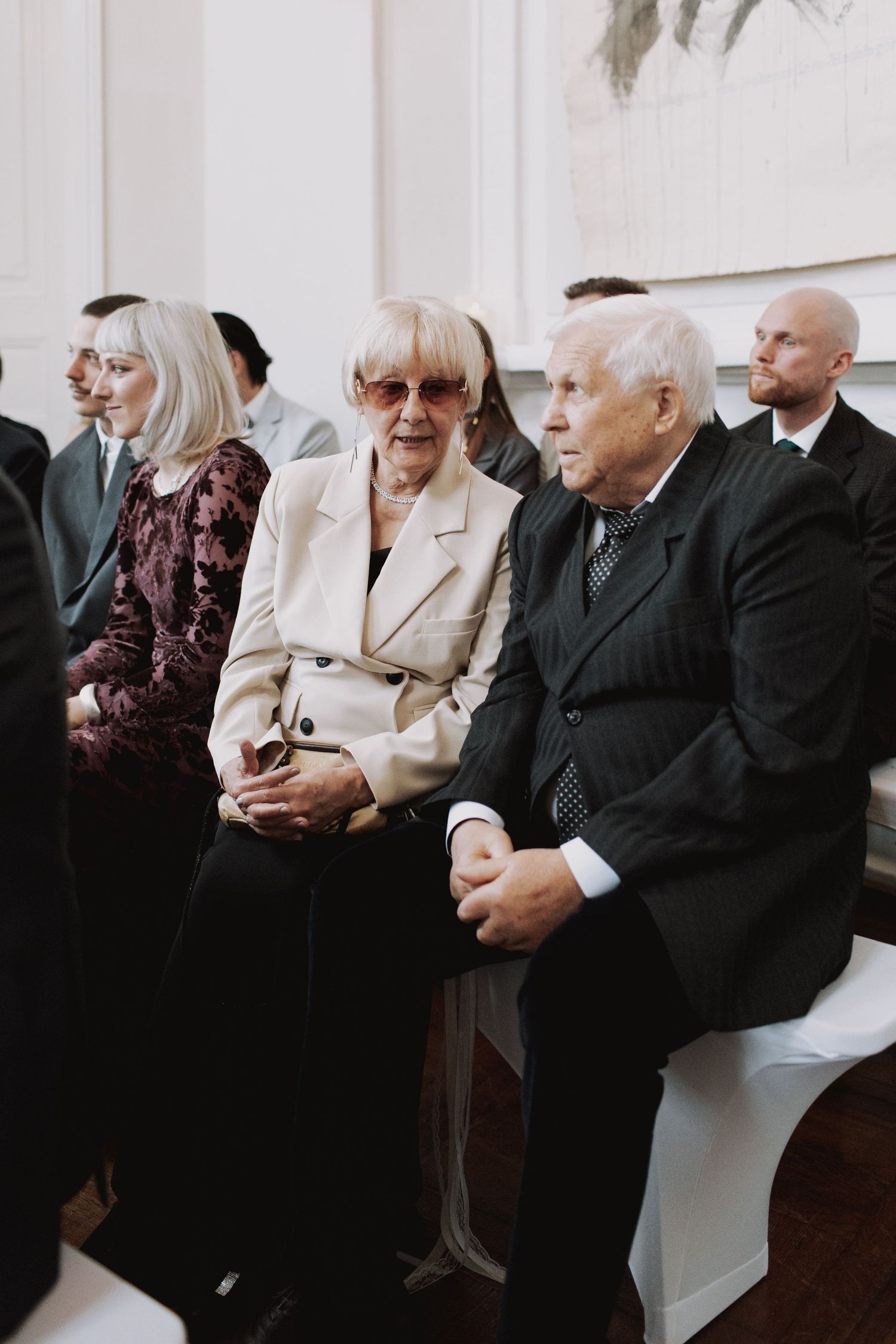 Wedding guests seated in formal attire at an indoor ceremony.