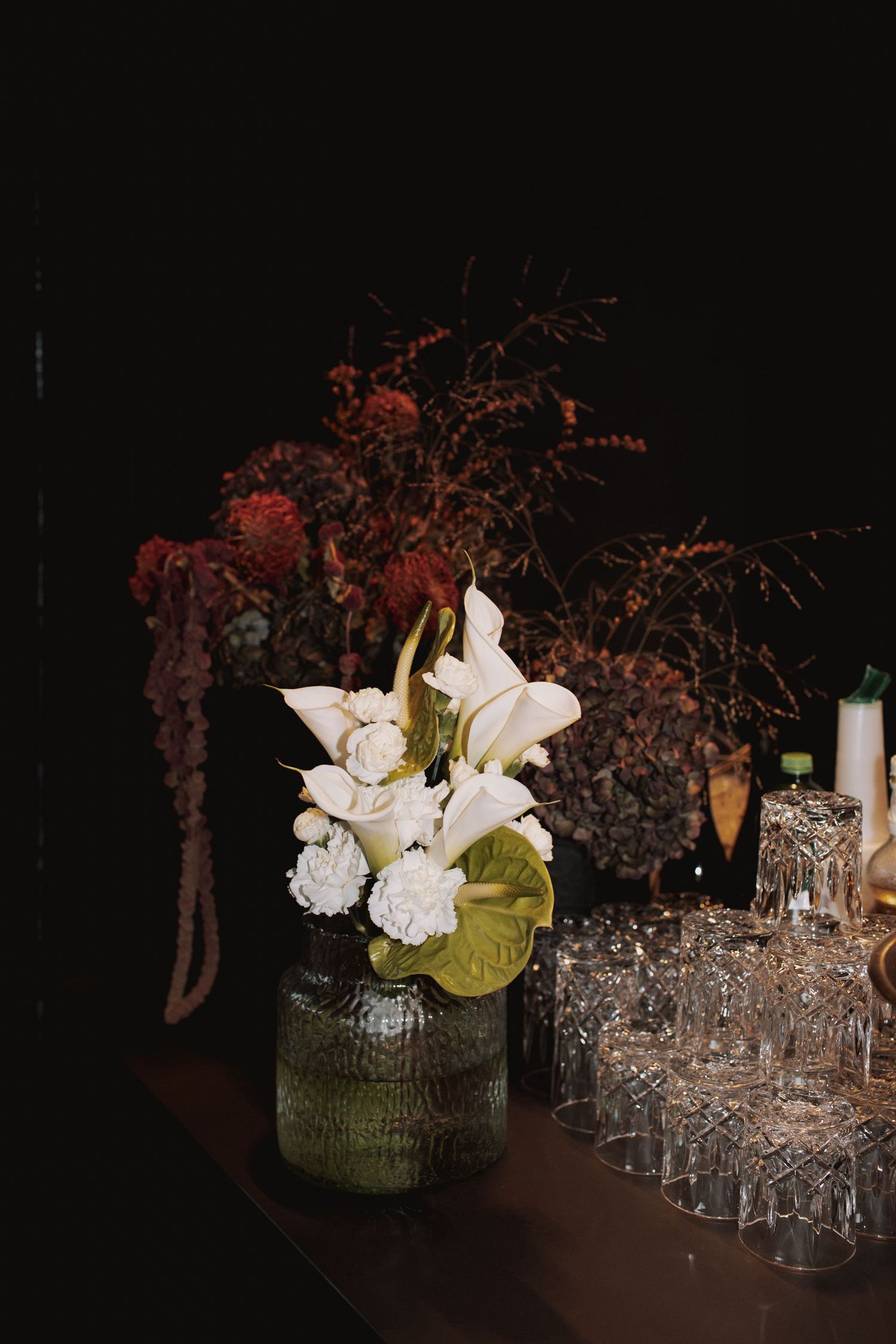 Floral centerpieces with white flowers and crystal glassware on dark table.