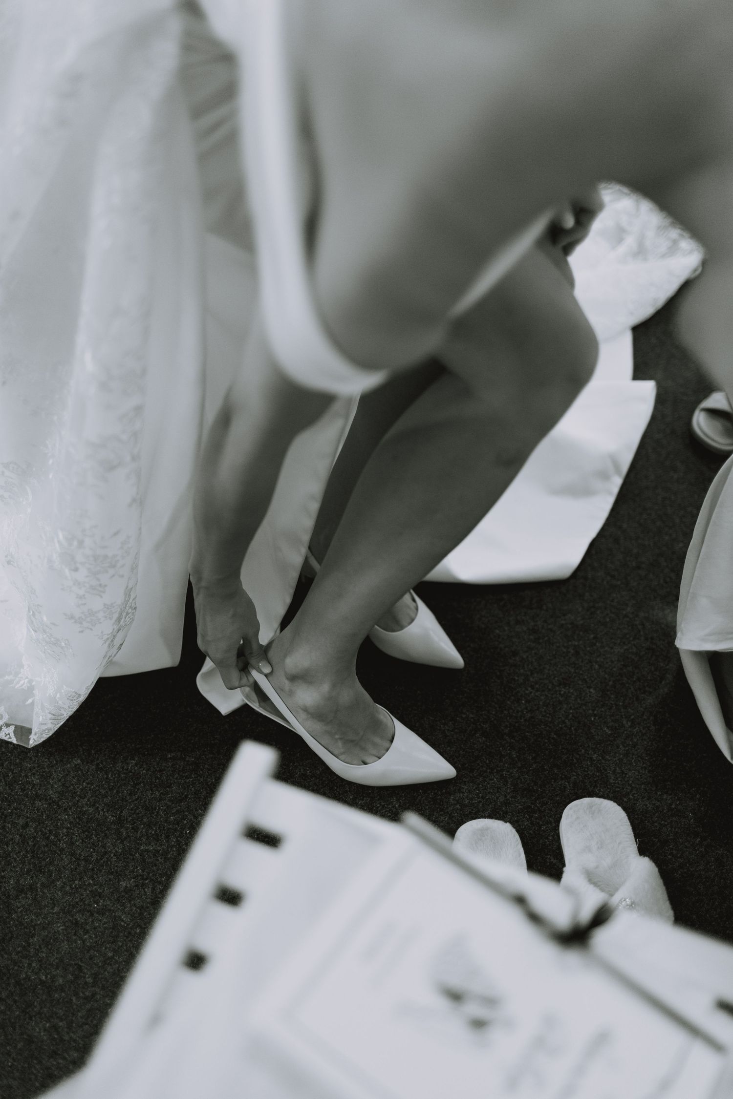 Black and white detail shot of formal shoes and dress hems on dark flooring.