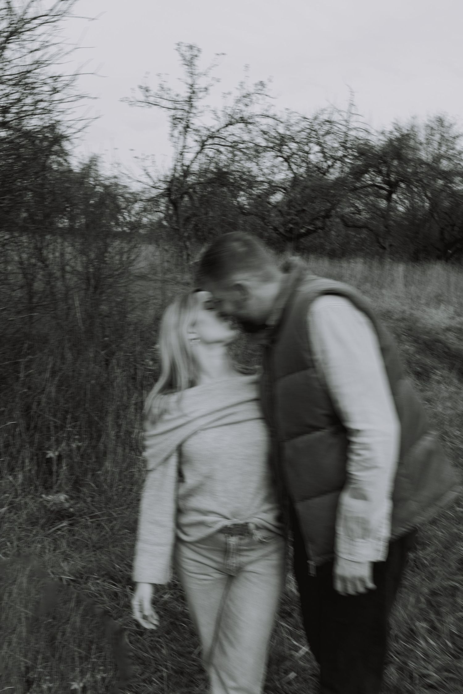 A blurred sequence of black and white photos showing two figures moving through tall grass in a field.