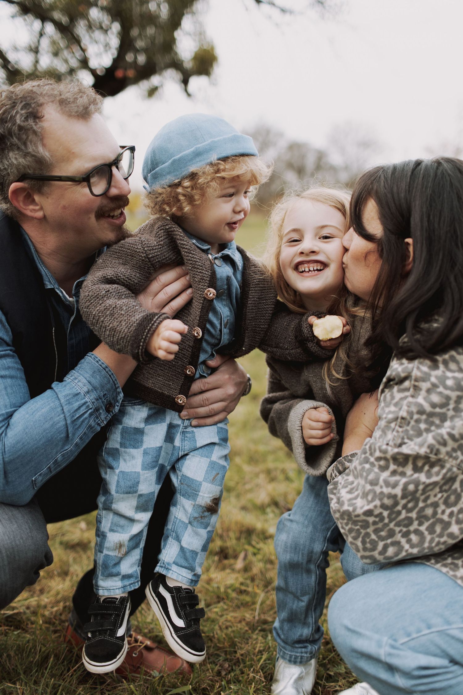 A family shares joyful laughter and embraces while sitting together outdoors on a cloudy day.