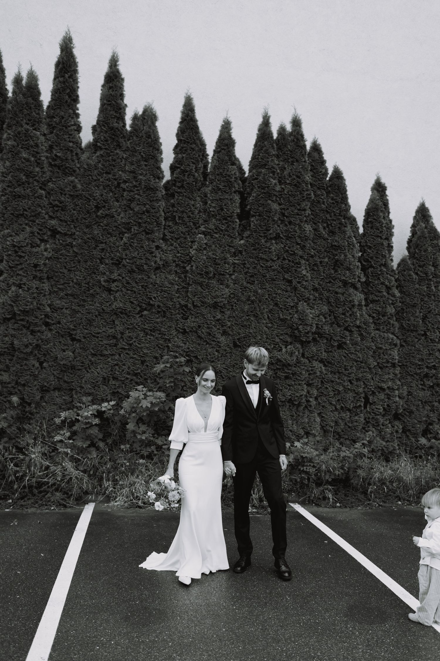 Wedding couple walking along a path lined with tall cypress trees.