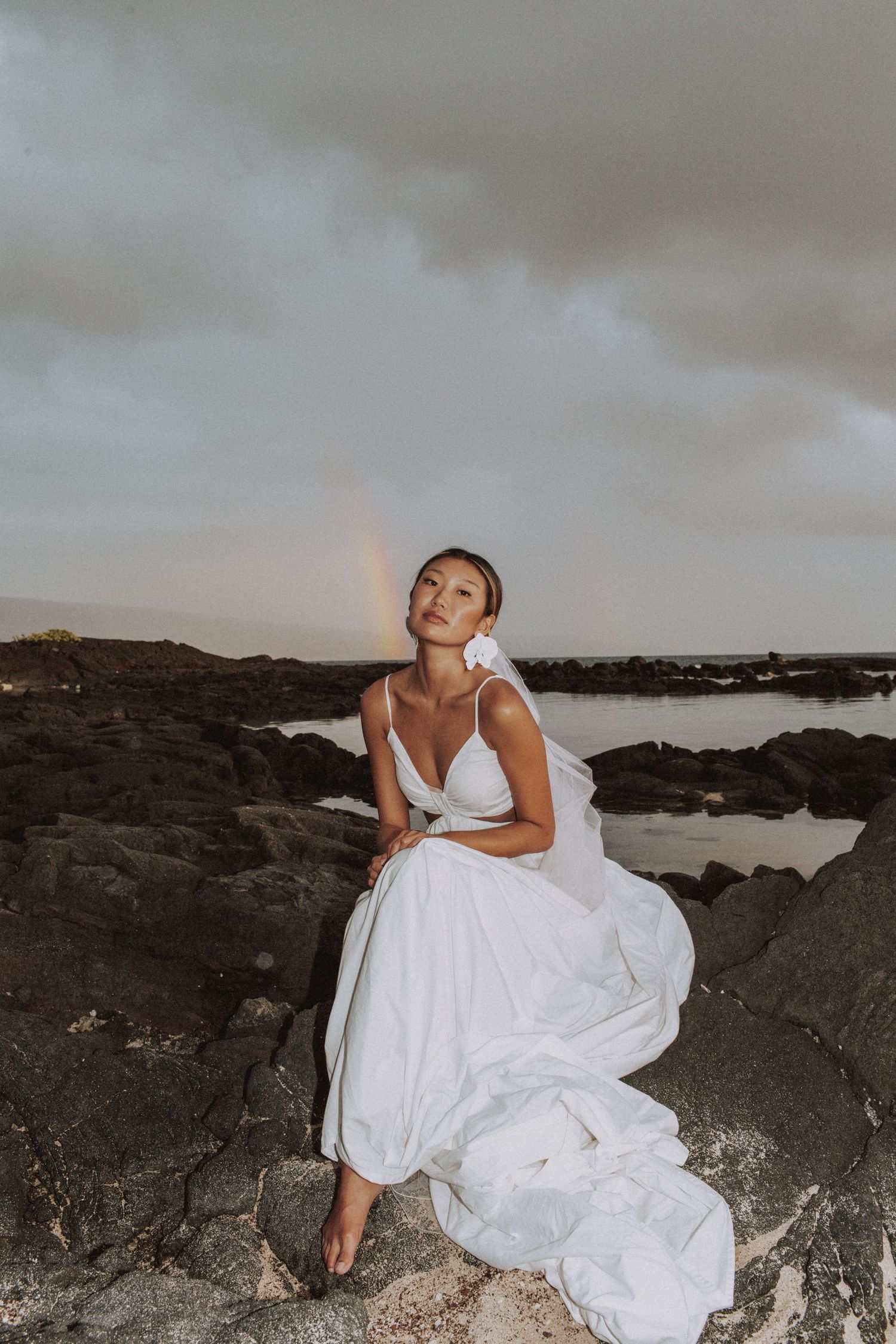 Moody bridal portraits on dark rocky coastline under cloudy skies.