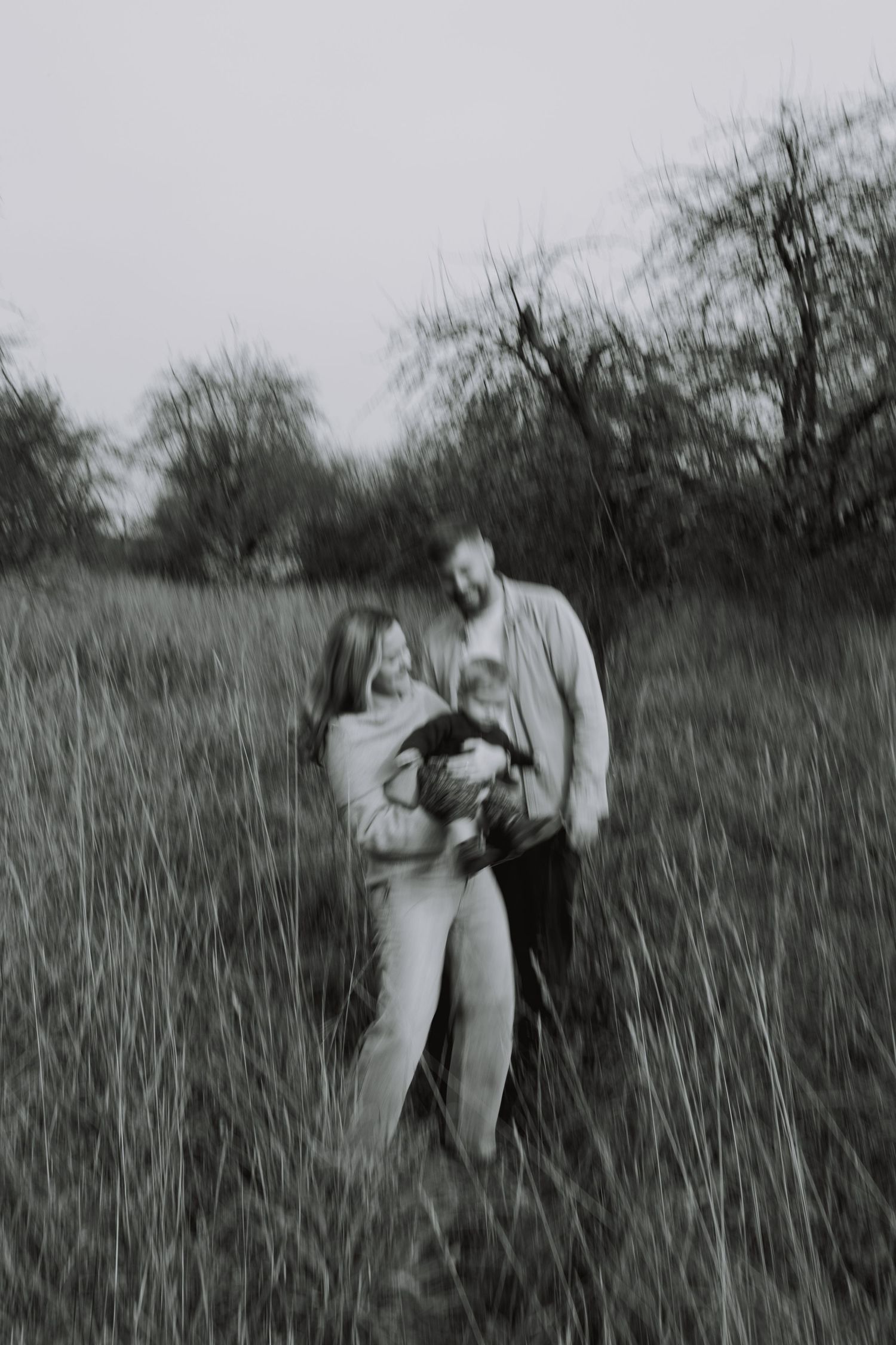 Black and white photograph showing two people embracing in a field of tall grass.