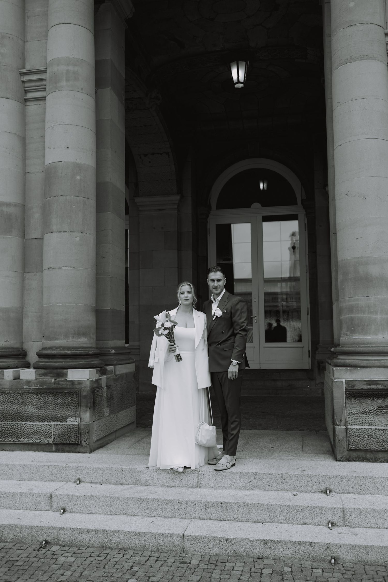 A wedding couple stands on the steps of a grand building with classical columns.