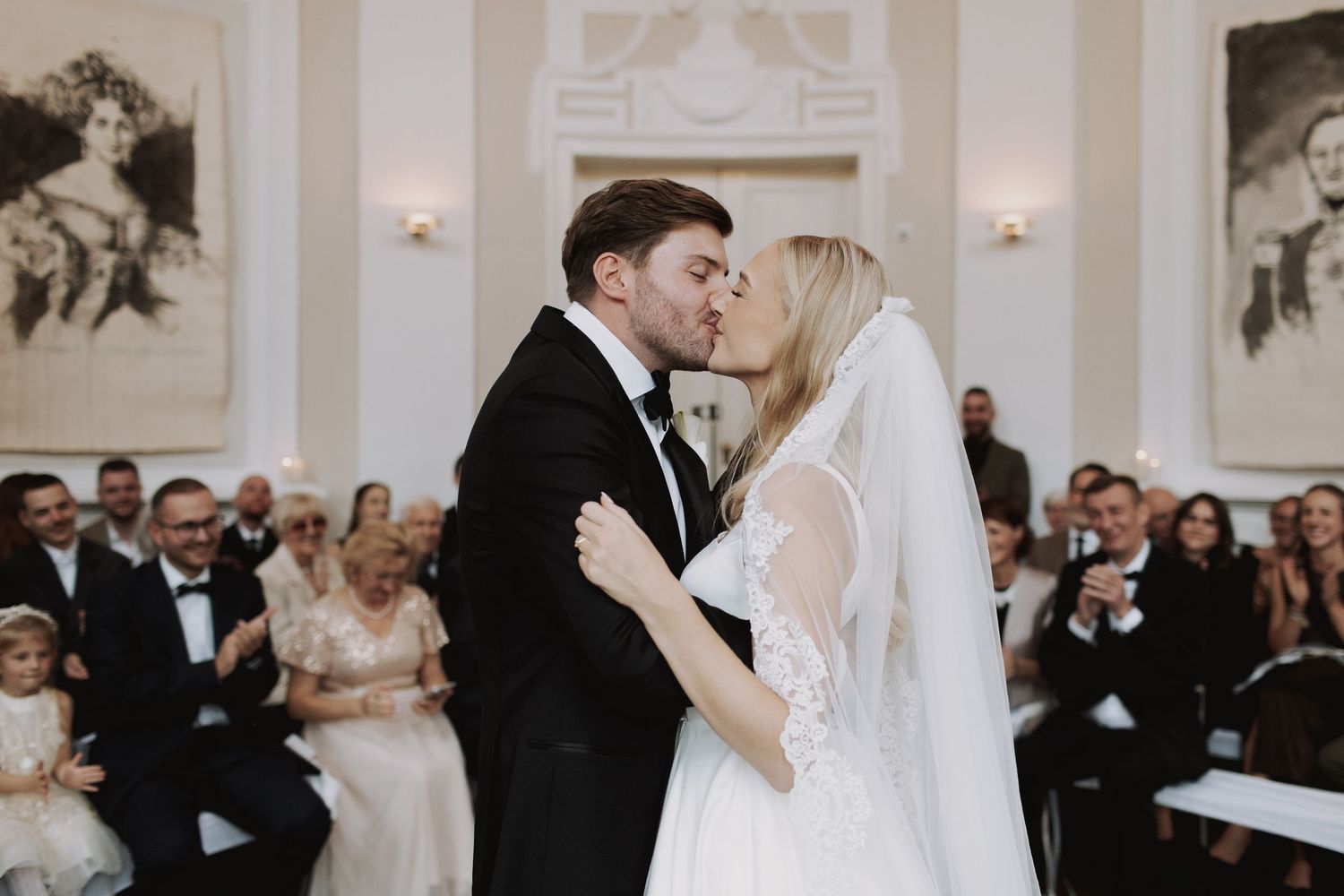 Wedding ceremony in a bright indoor venue with white walls and formal decorations.